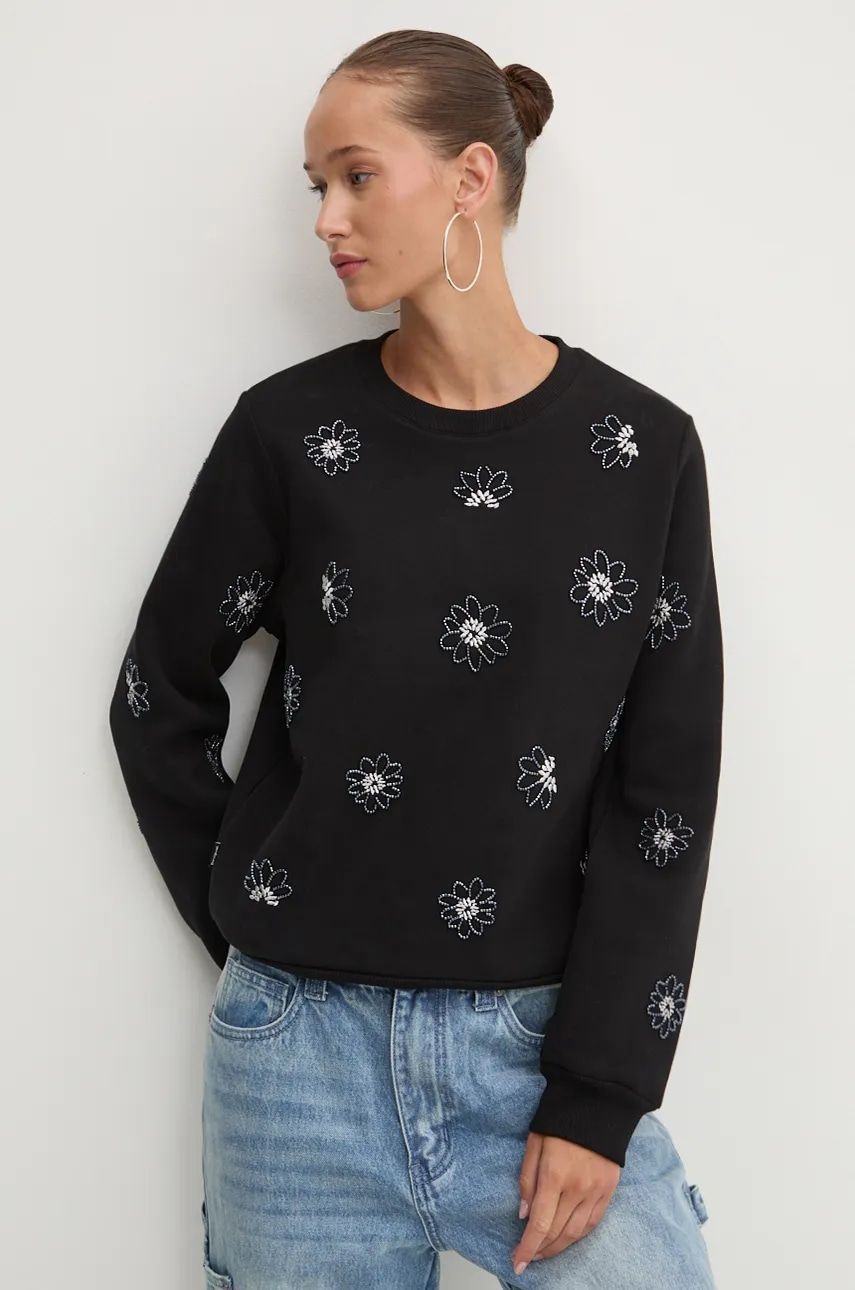 Donna con felpa nera a fiori e jeans, che guarda di lato.