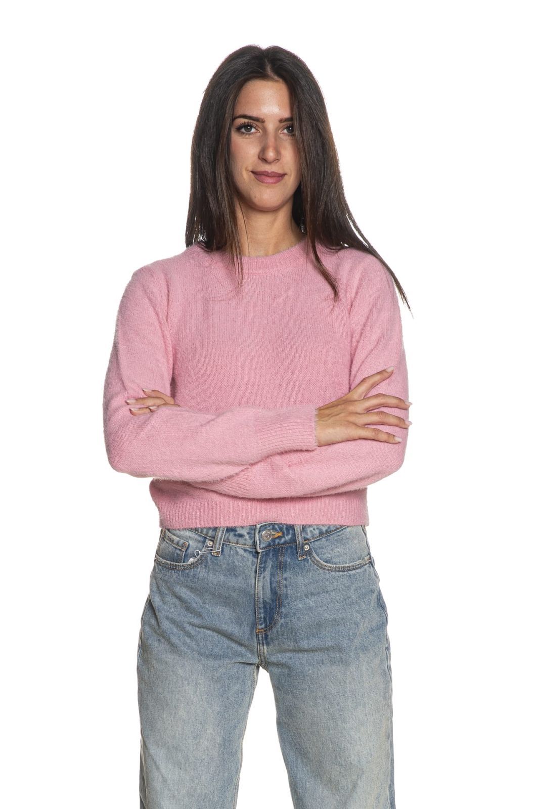 Donna con maglione rosa e jeans blu, braccia incrociate, che guarda la telecamera.