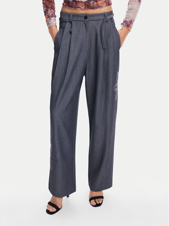 Donna che indossa pantaloni grigi a pieghe e tacchi neri, mani in tasca.