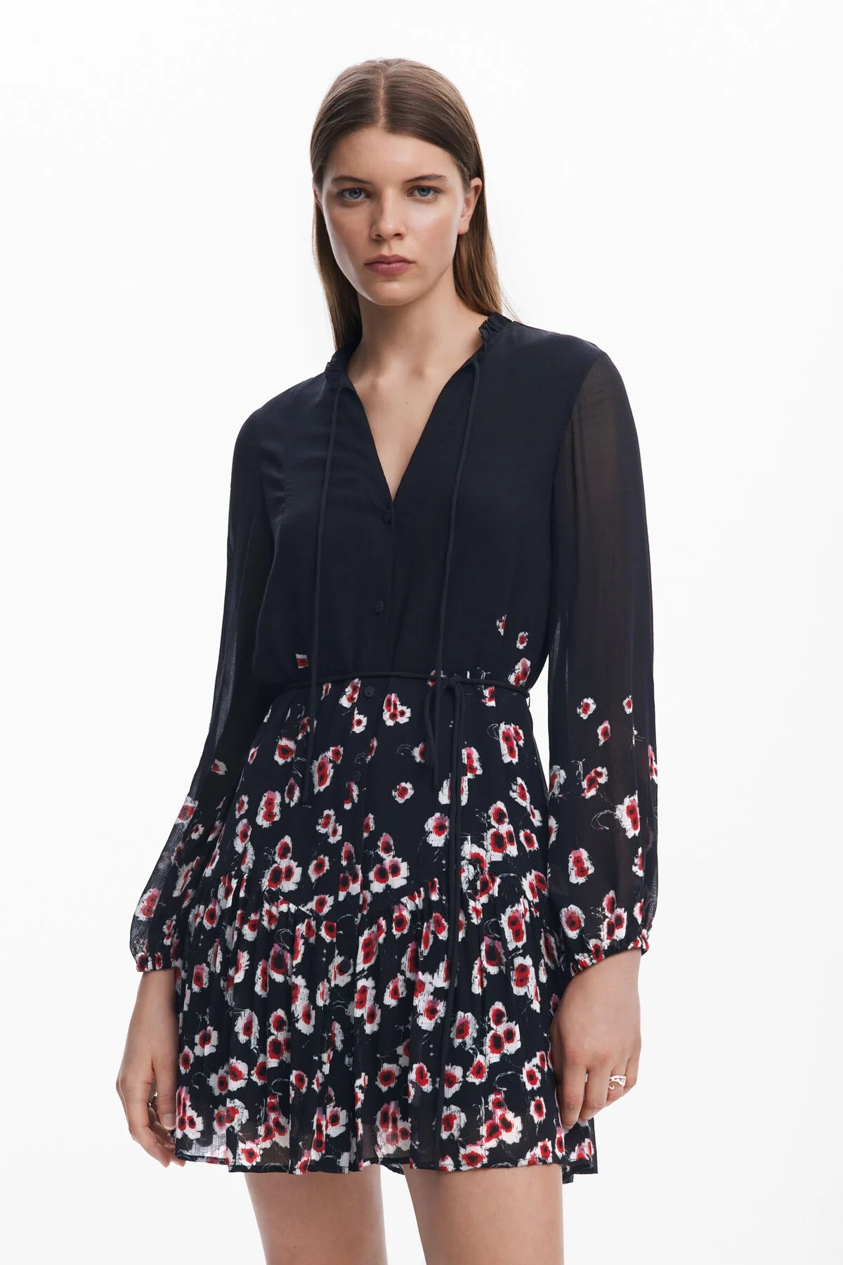 Donna in abito nero con gonna a stampa floreale, in piedi e con lo sguardo rivolto in avanti.