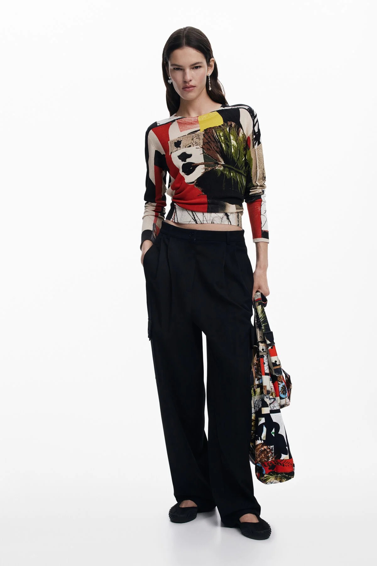 Donna in piedi con top con stampa astratta e pantaloni neri, che tiene una borsa.