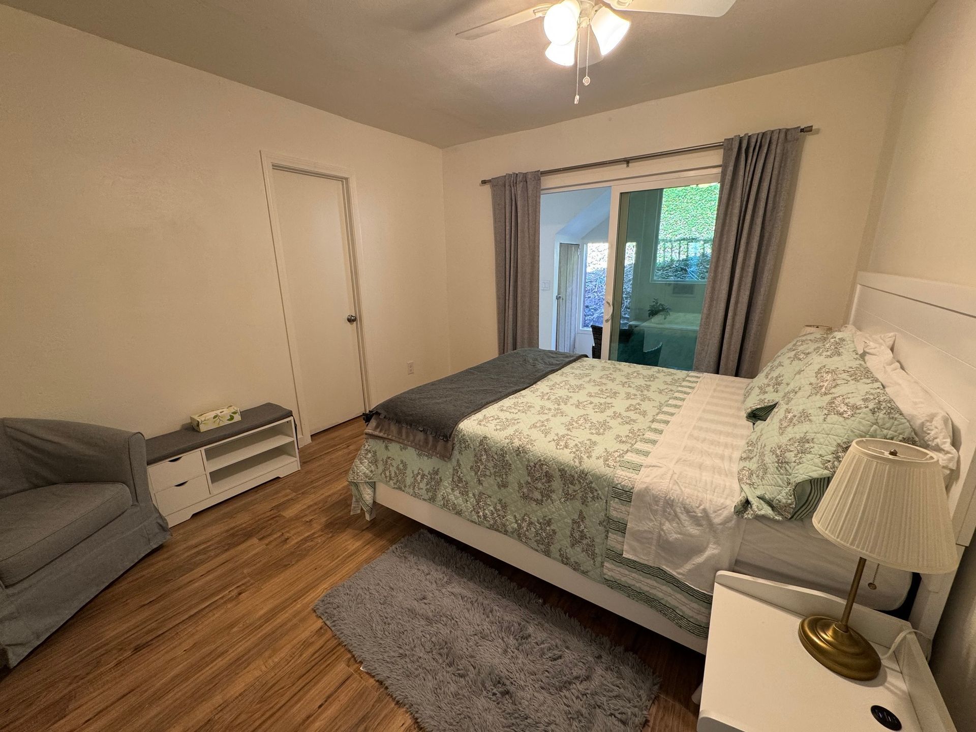 Bedroom with a white bed, doors to a balcony, and a small side table with a lamp.