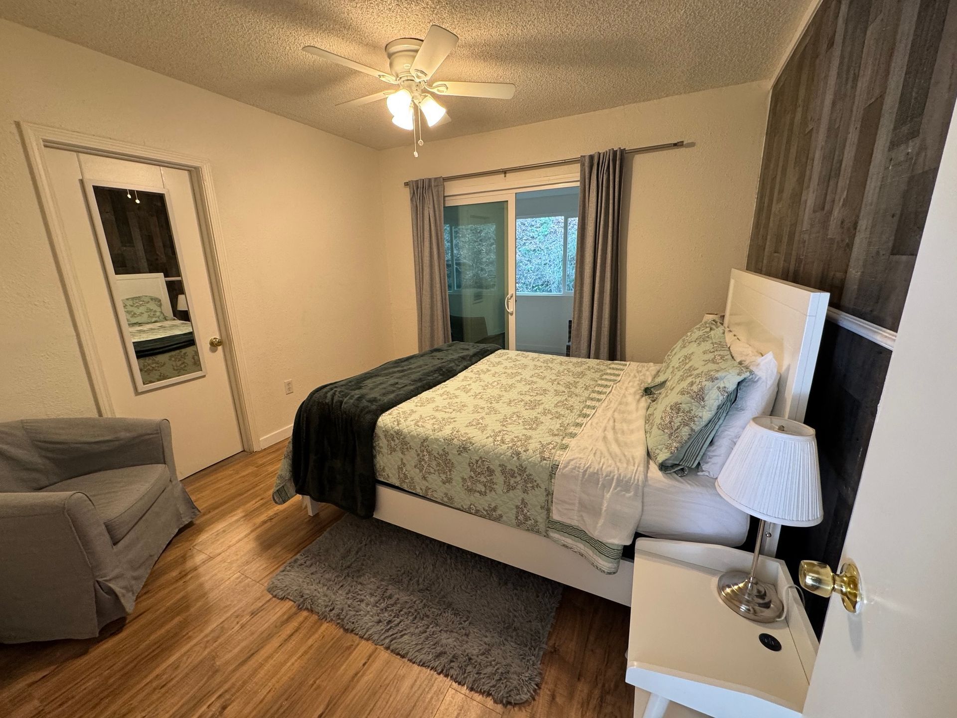 Bedroom with a white bed, doors to a balcony, and a small side table with a lamp.