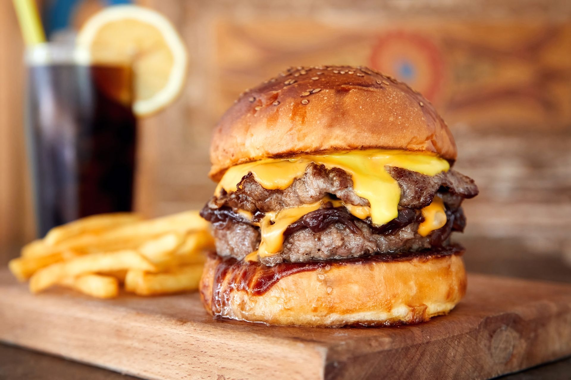Double cheeseburger, fries, and cola on a wooden board.