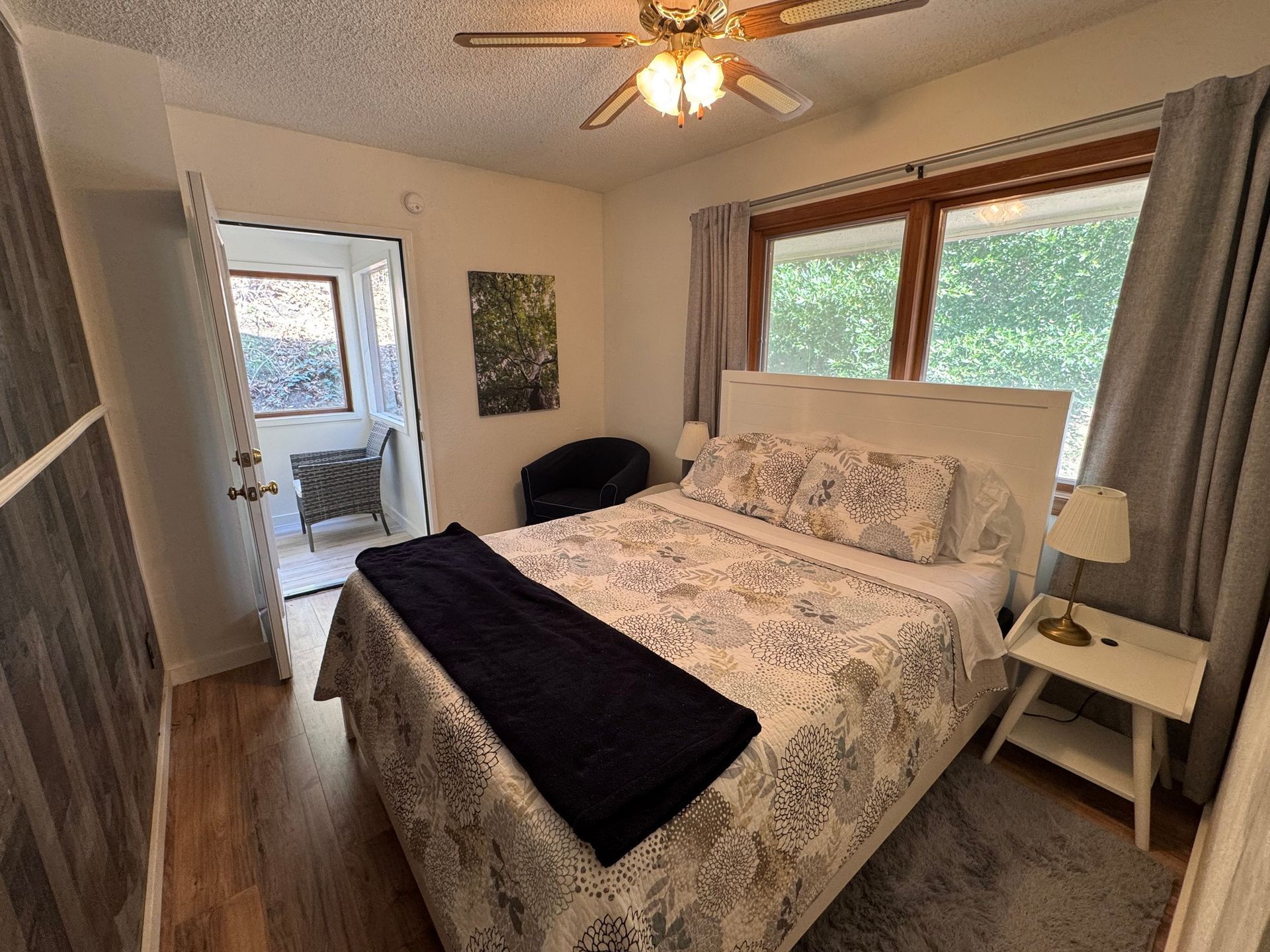 Bedroom with a white bed, doors to a balcony, and a small side table with a lamp.