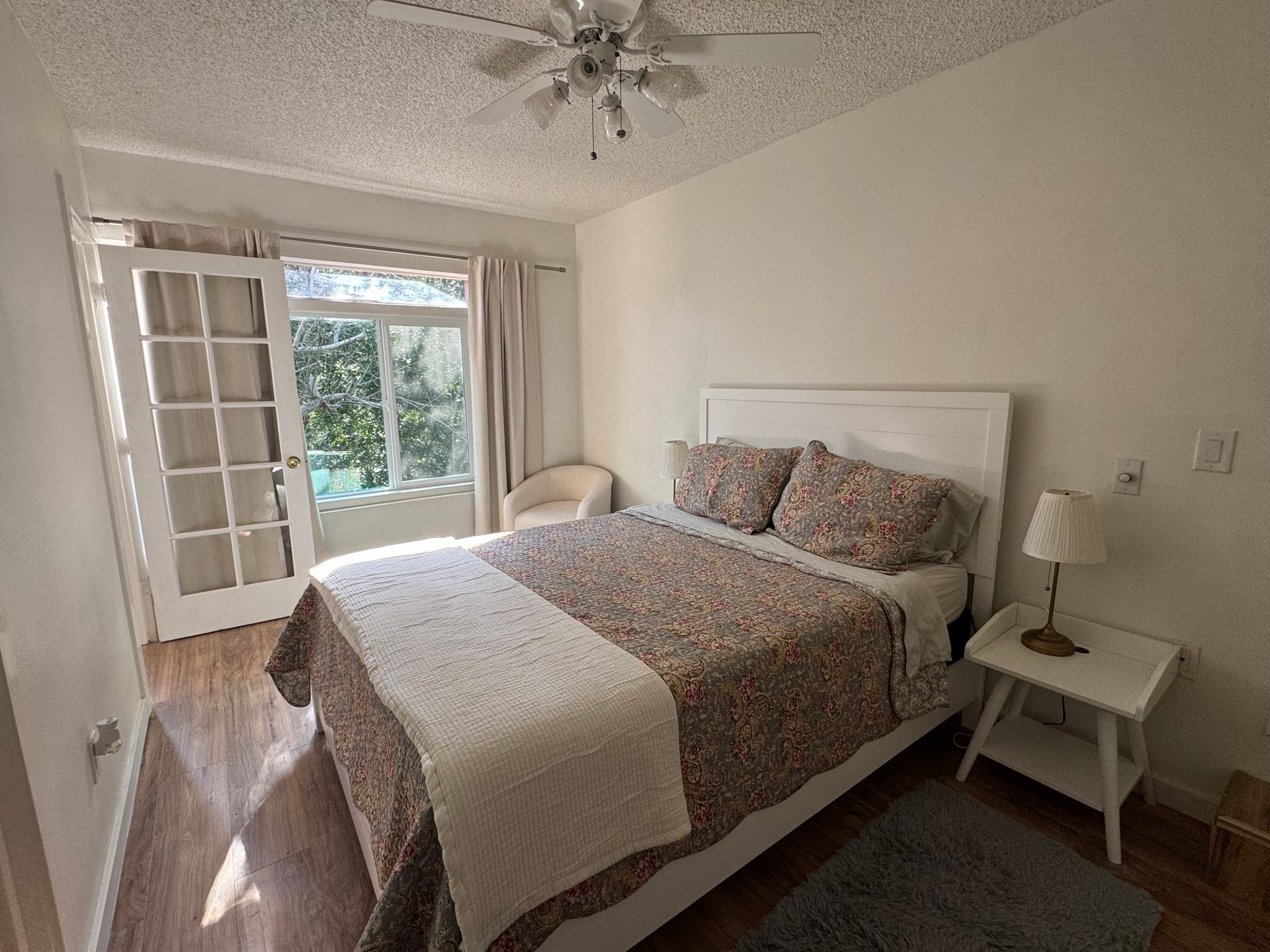 Bedroom with a white bed, doors to a balcony, and a small side table with a lamp.