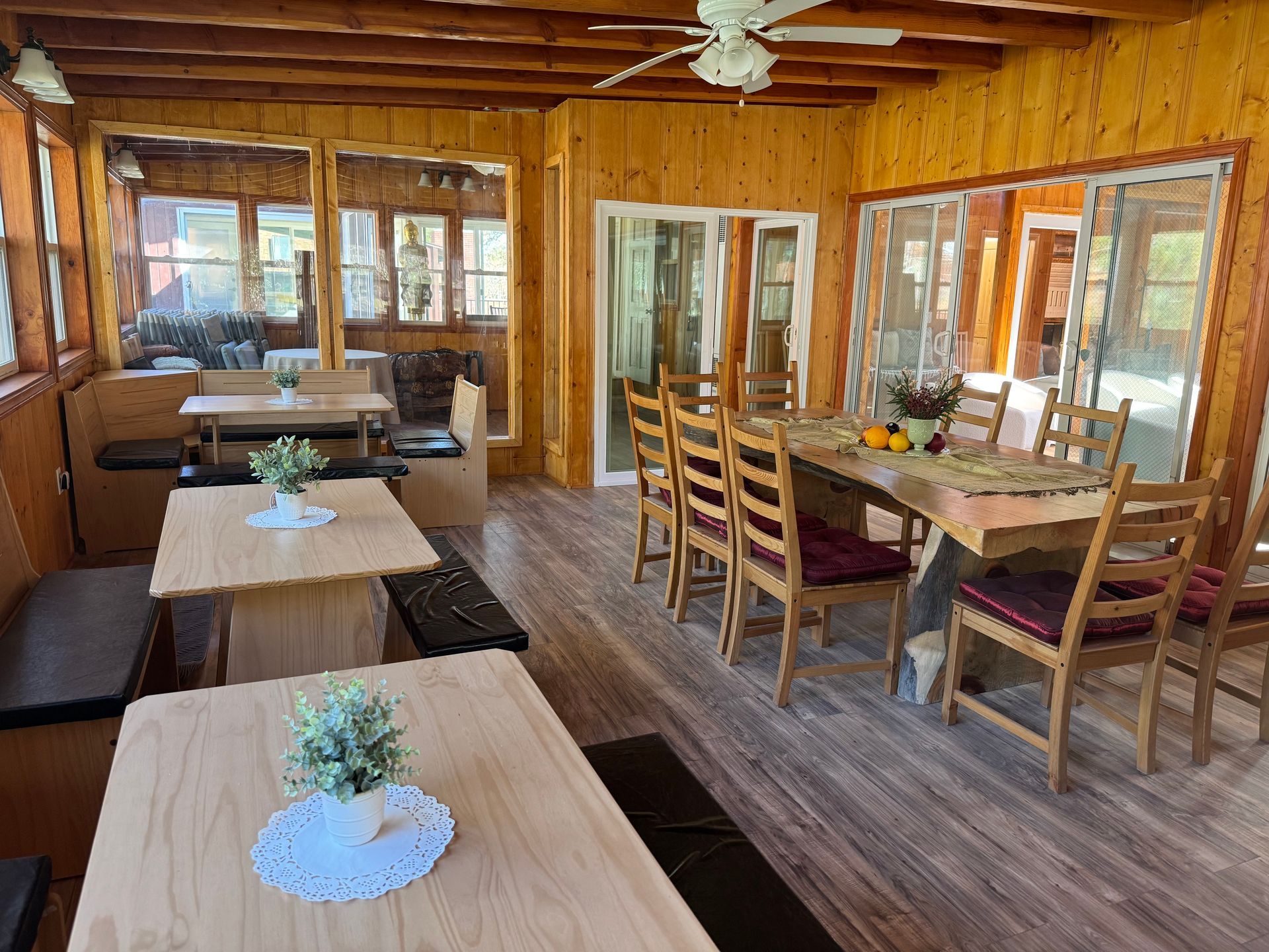 A wood-paneled room with multiple dining tables, chairs, booth seating, and large windows looking outside.