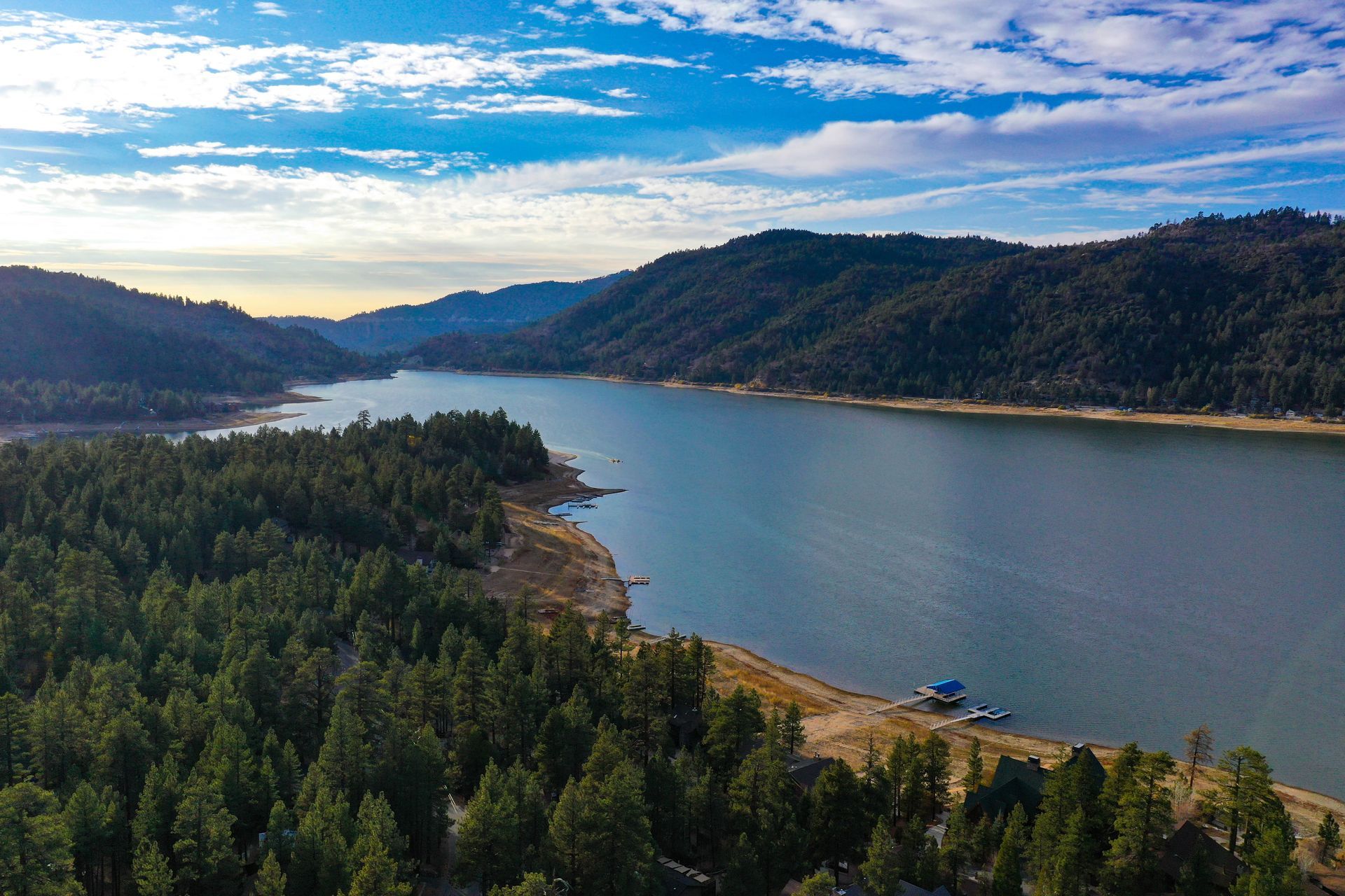 Wide river or lake winding through forested hills under a blue, partly cloudy sky