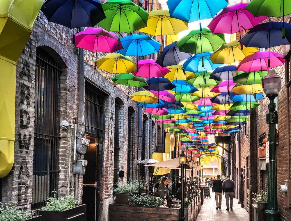 Palm trees frame a city, with buildings and mountains in the background, lit by the golden hour.