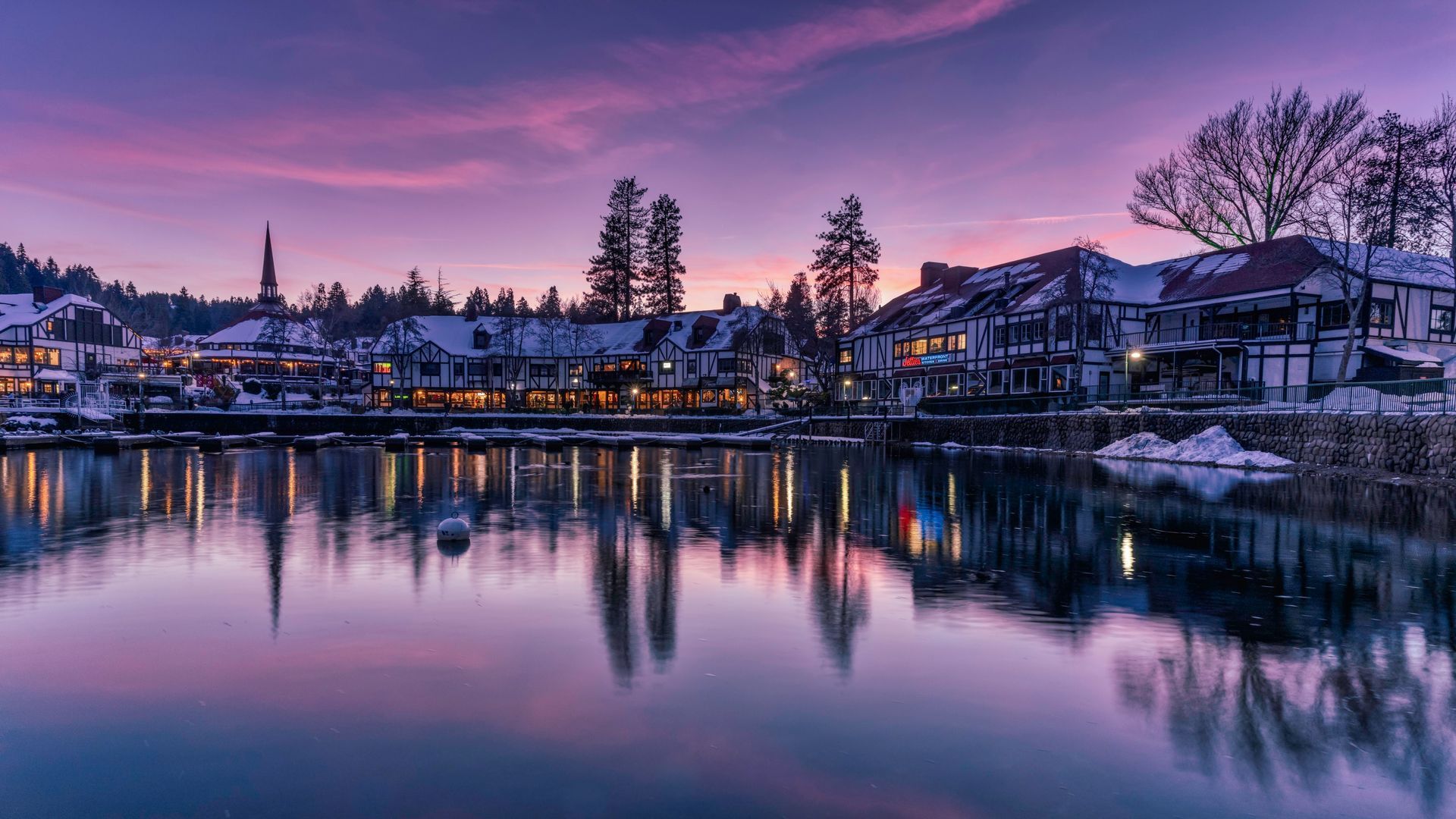 Twilight lakeside town with purple sky and lit buildings reflected in calm water