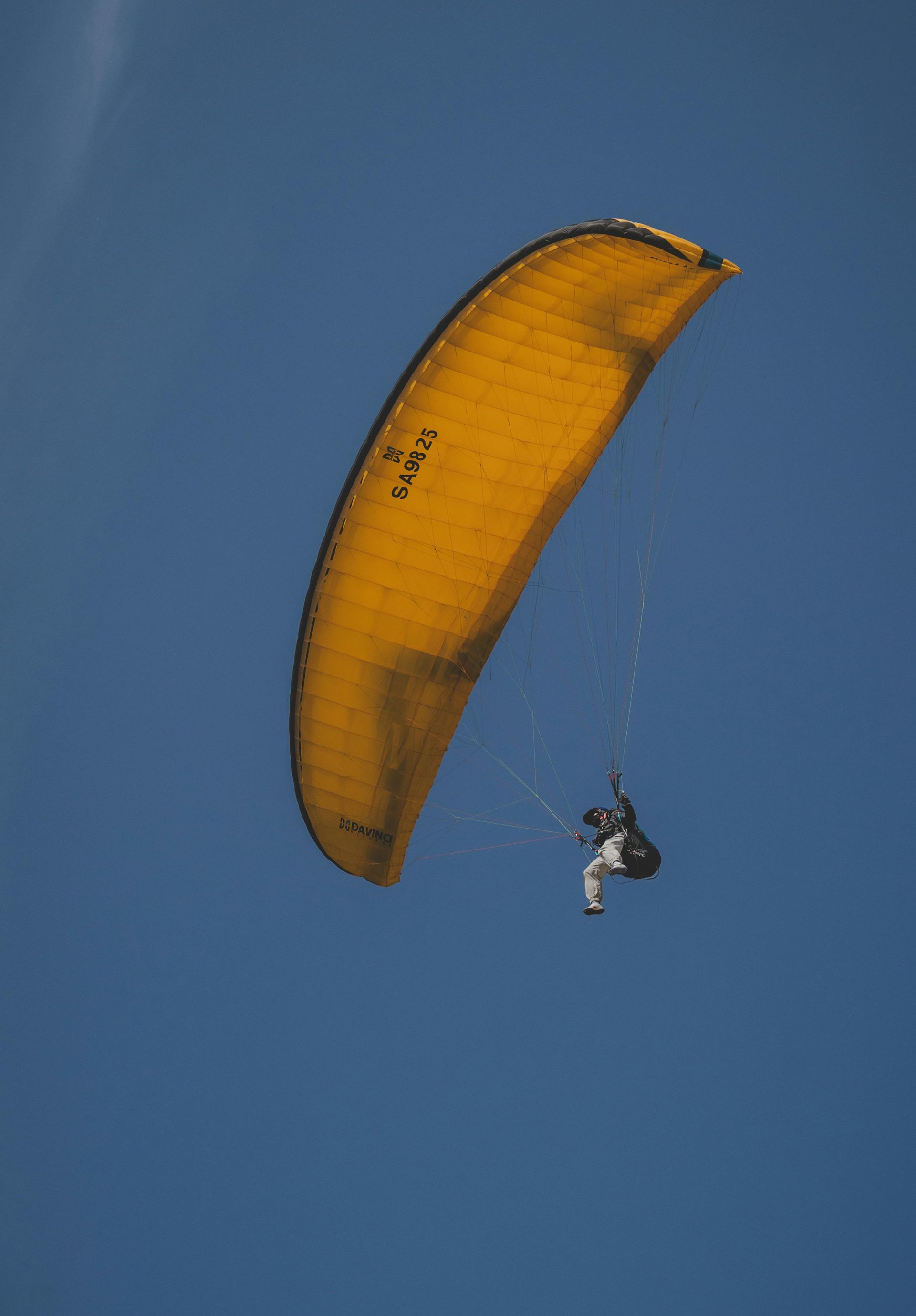 A person paragliding beneath a large, vibrant yellow canopy against a clear blue sky.