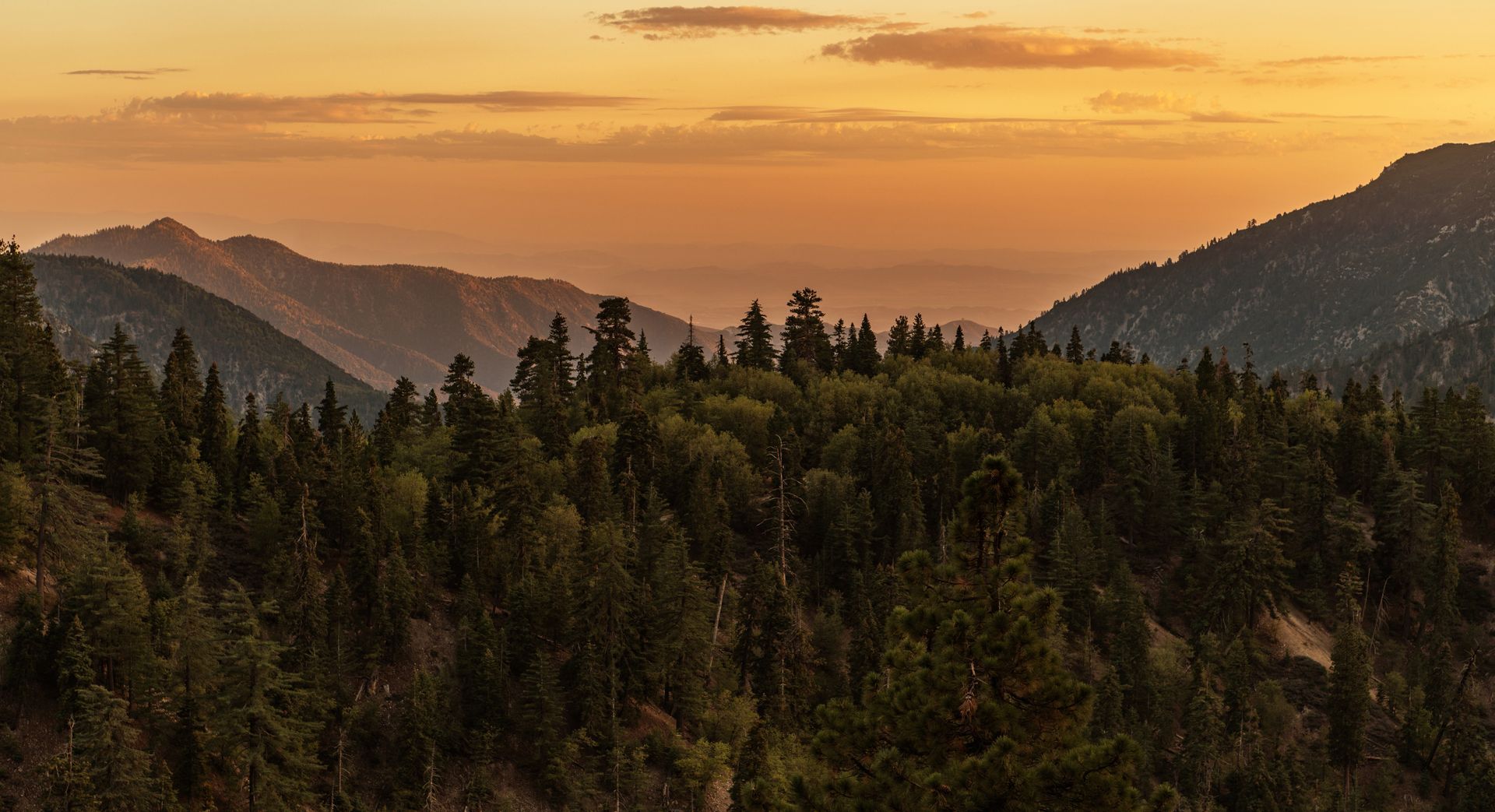 Sunset over forested mountains with orange sky and distant ridges