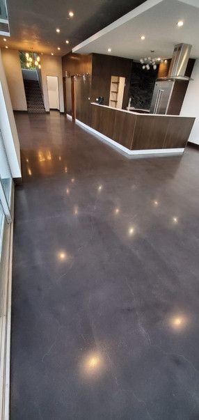 A large room with a black floor and a kitchen in the background.