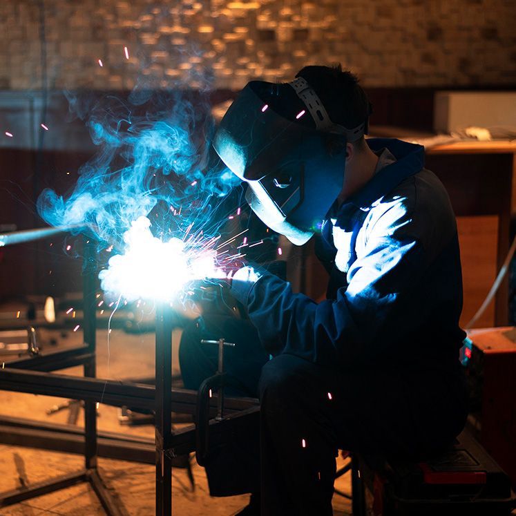 Welder in protective gear at work, using a torch with bright blue sparks.