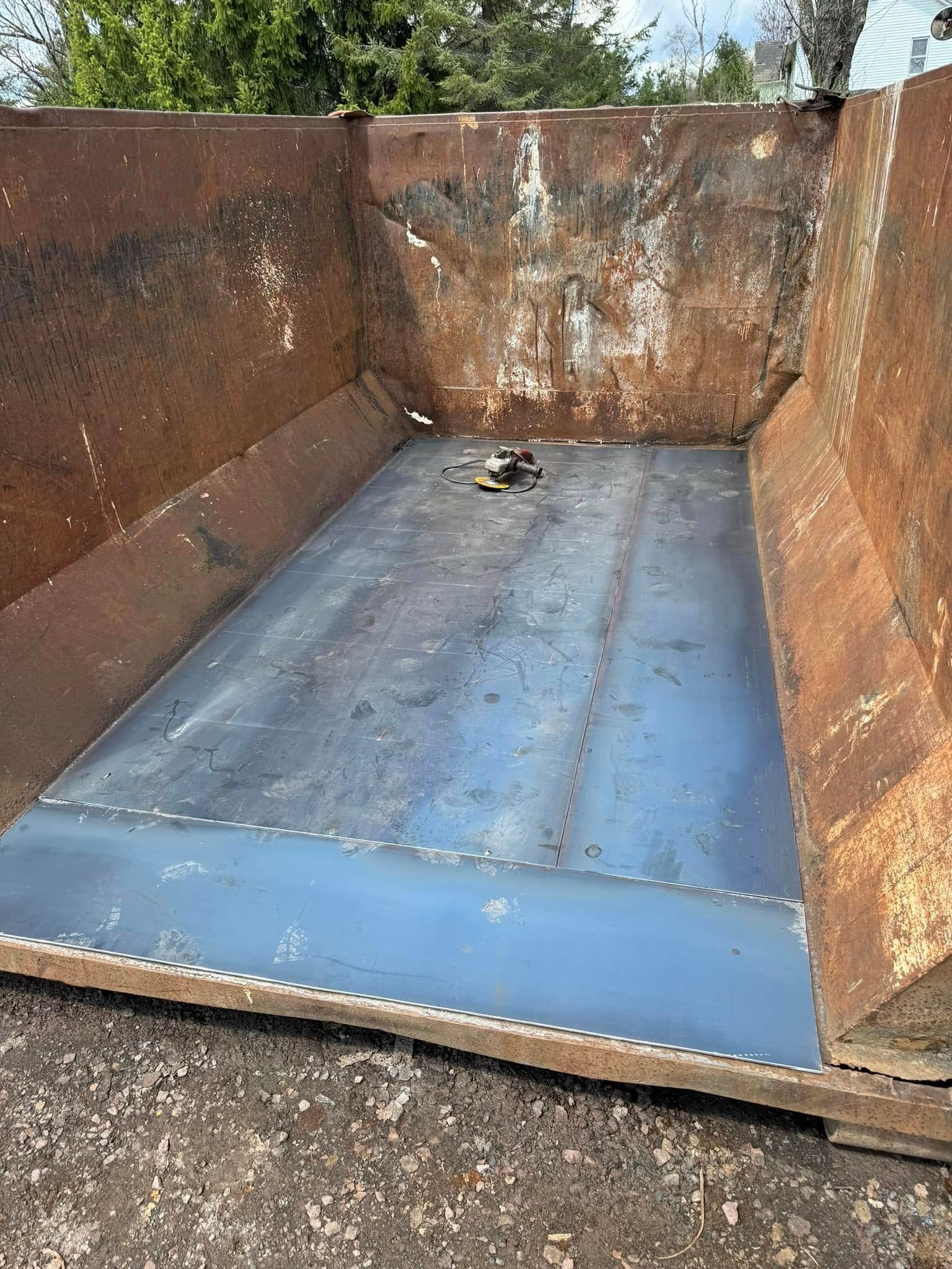 Empty, rusty dumpster with a recently welded blue metal floor.