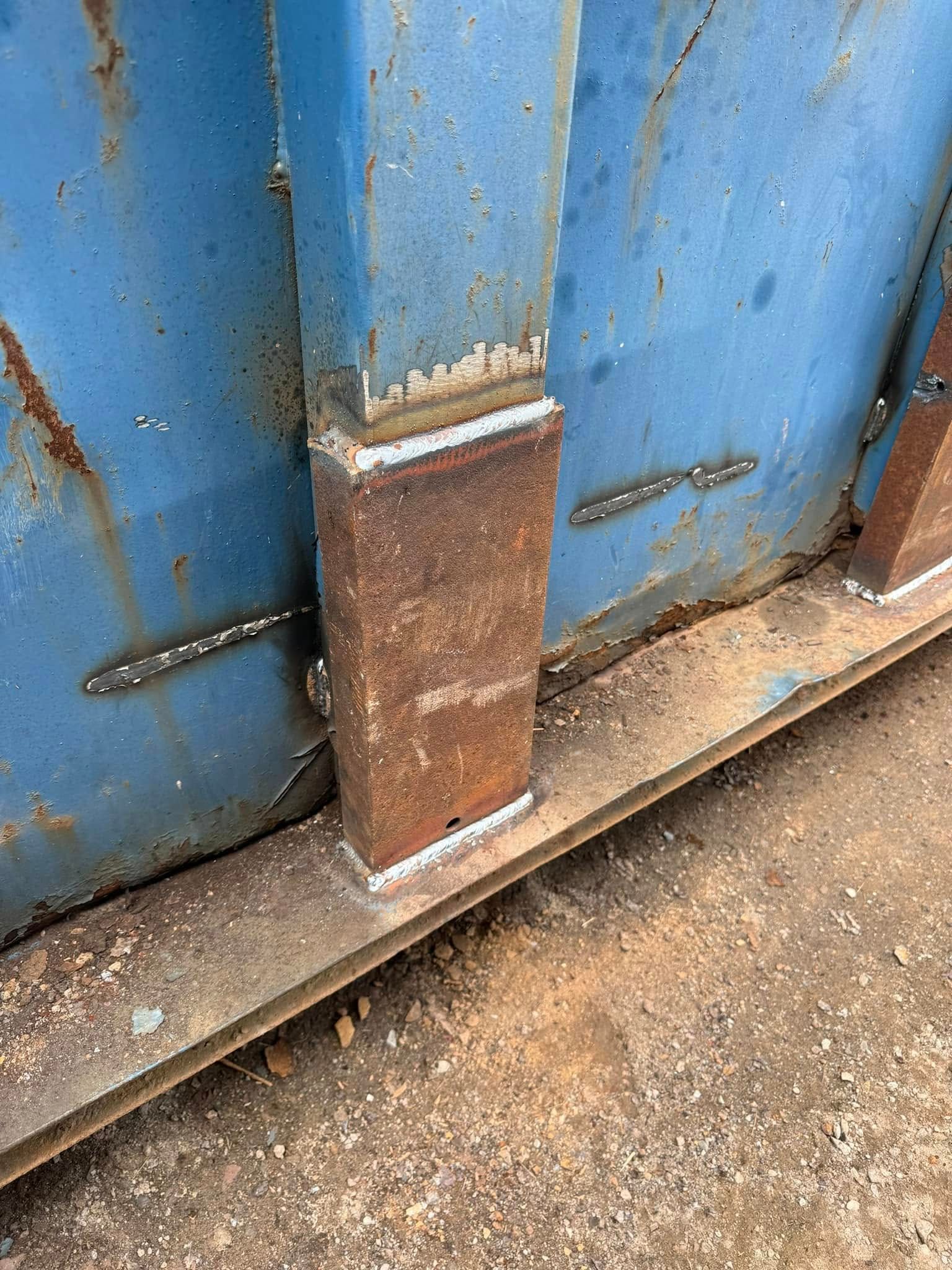 Rusty metal post welded to a blue metal structure.