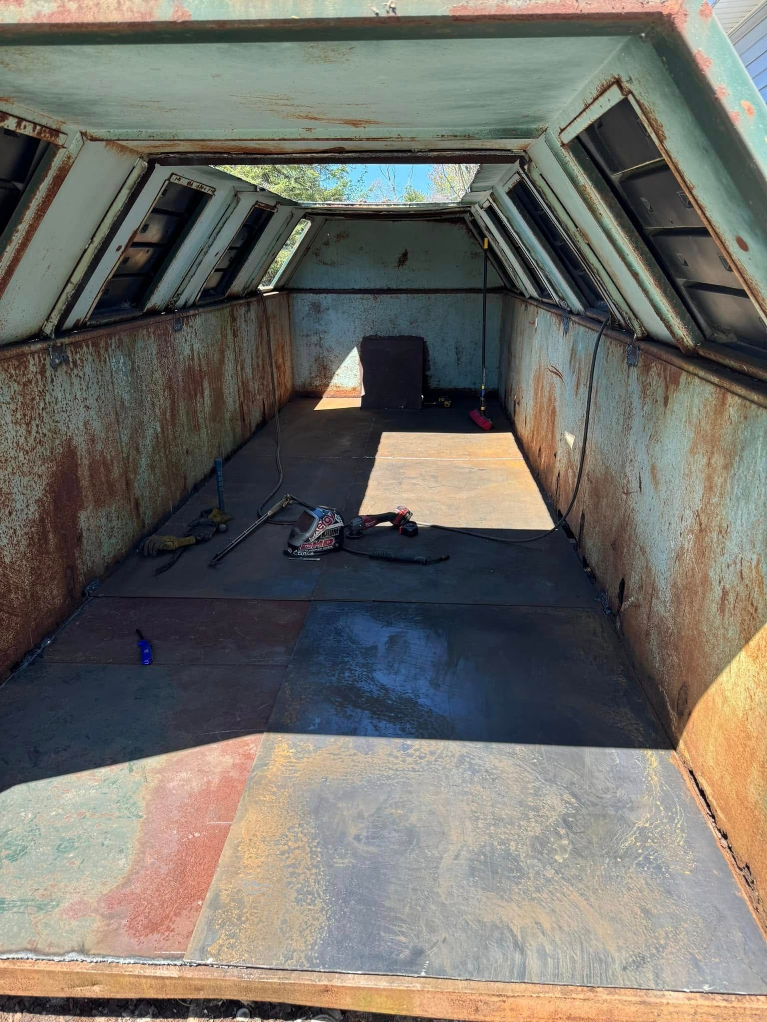 Interior of a rusty, green metal structure with open roof.  Debris and a small square object sit on the floor.