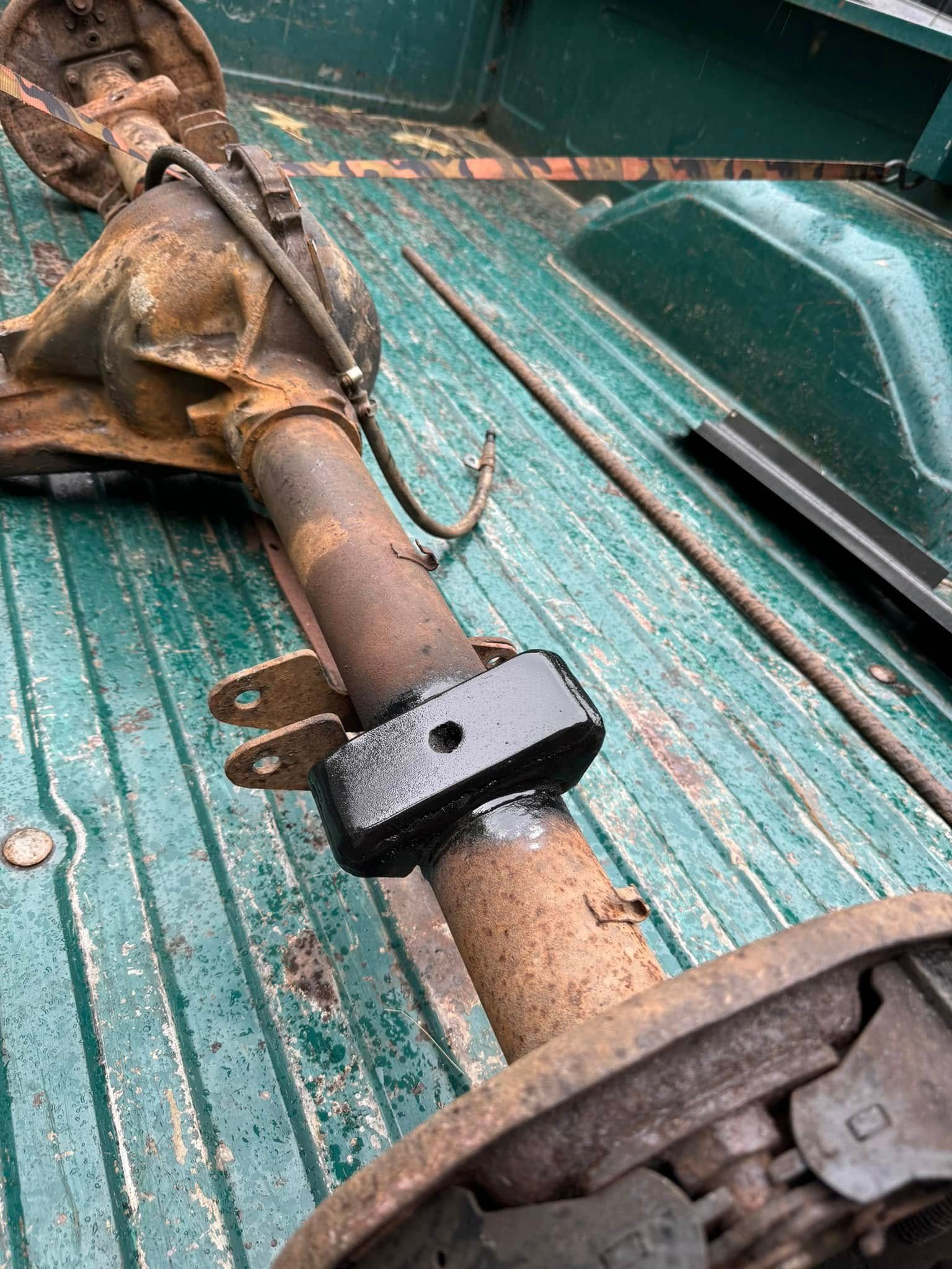 Rusty rear axle with a black bracket in a truck bed.