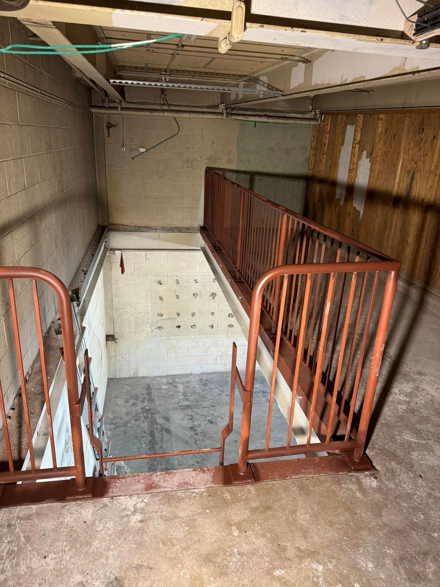Basement with descending stairs, rust-colored railings, and cinder block walls; unfinished, concrete floor.