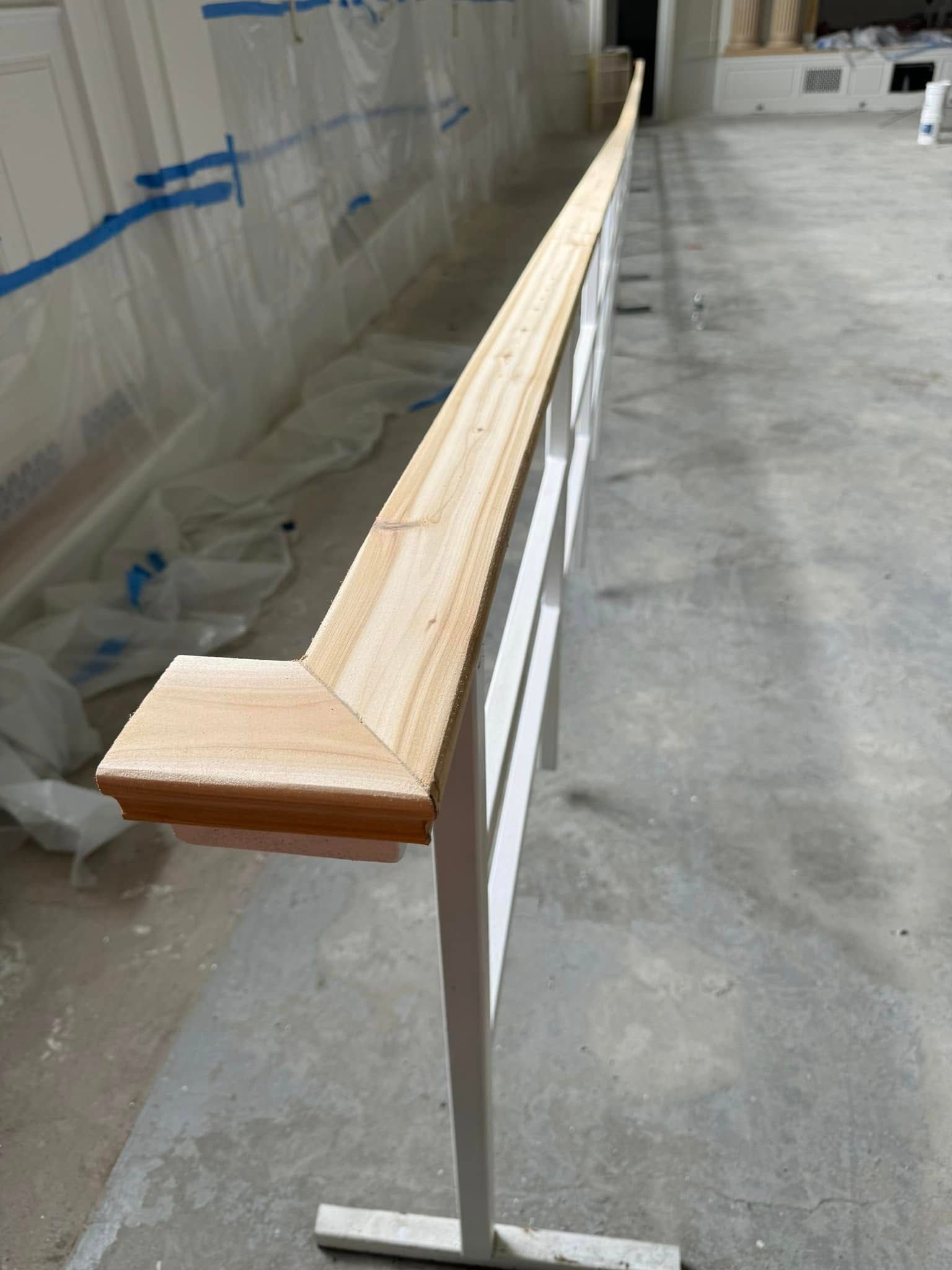 Wooden handrail on white support, unfinished, in a building interior.