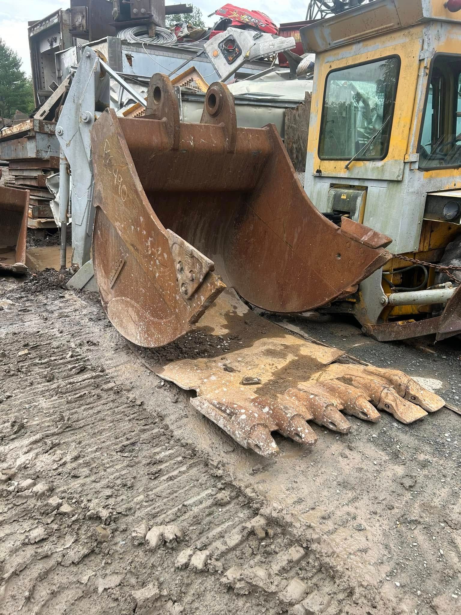 A large, rusty excavator bucket on muddy ground near a yellow machine.