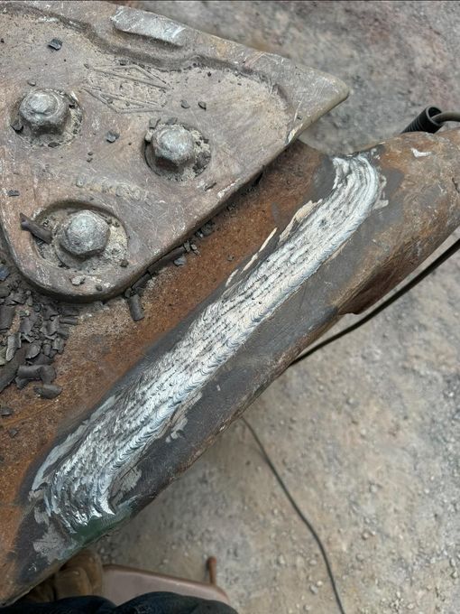 Welded metal joint on a rusty surface, with visible weld beads and bolted connection.