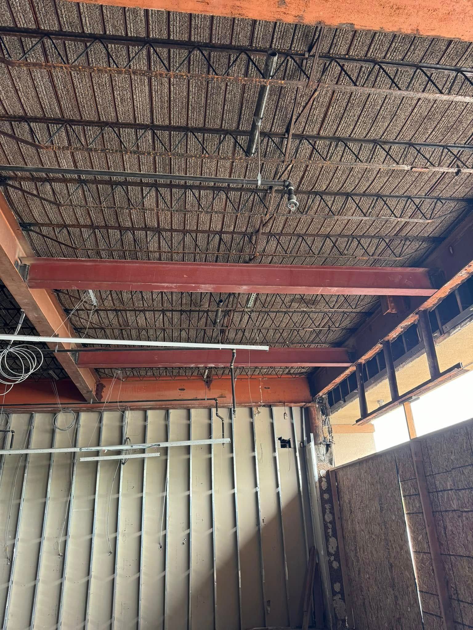 Steel beams support a ceiling with exposed rebar and wiring, interior building construction.