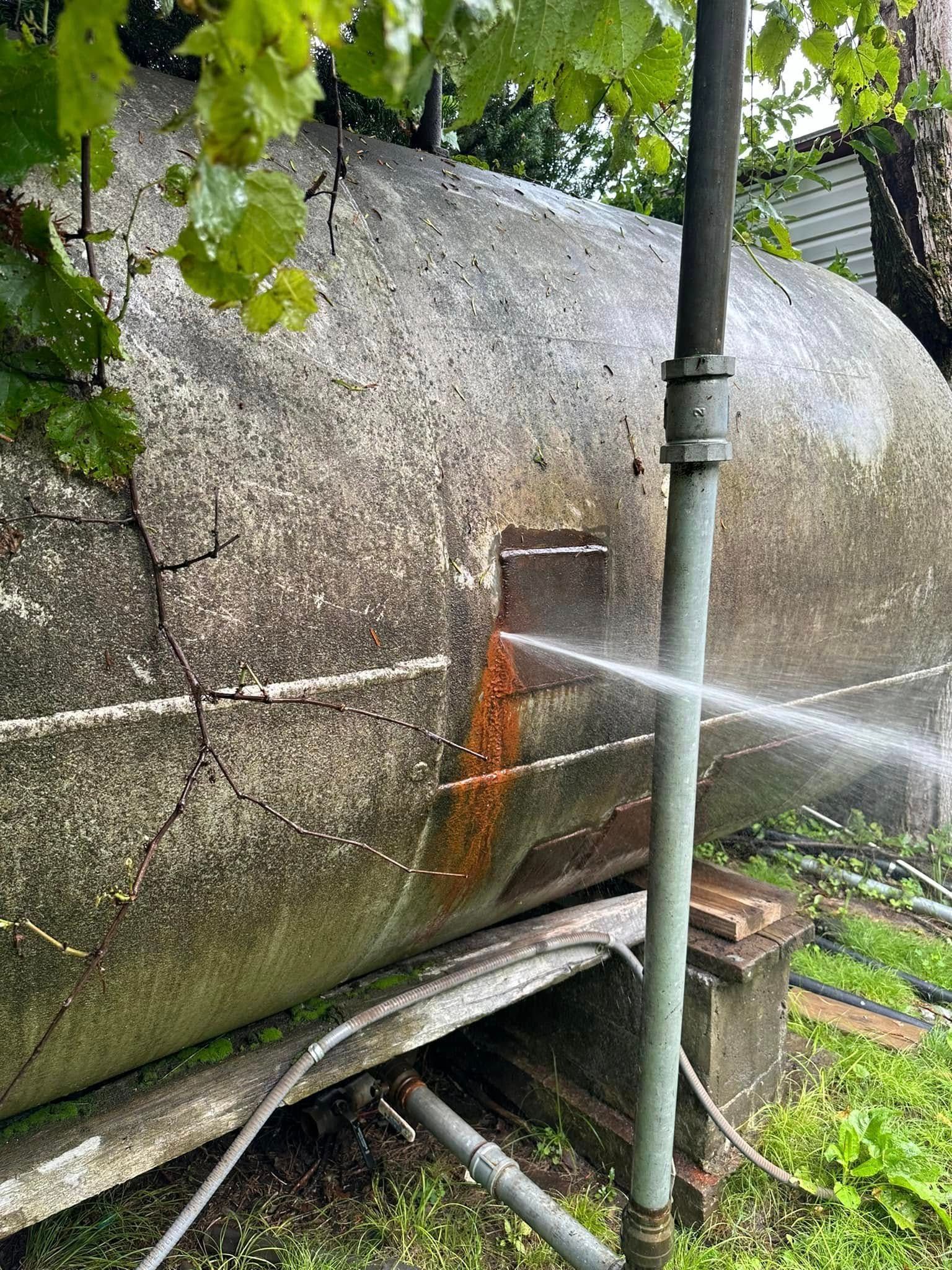 Water spraying from a hole in a large, weathered, horizontal concrete tank.