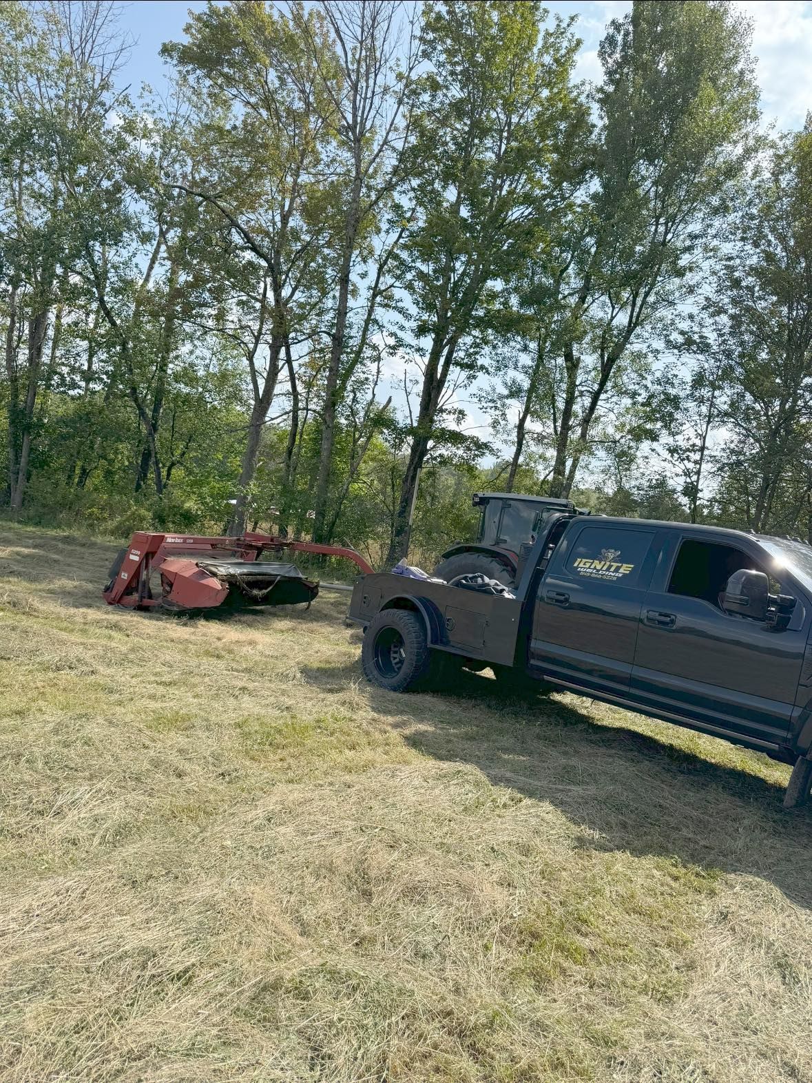 A brown truck pulling a red mower in a field of cut grass, trees in the background.