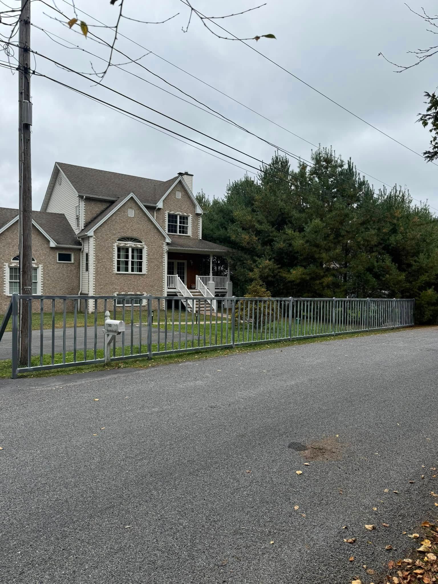 Gravel driveway leading to a two-story stone house with a front porch; overcast day.