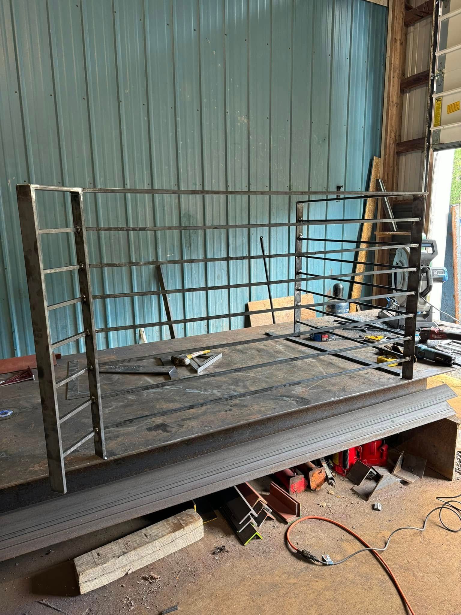 Welded metal gate frame on a flatbed. Workshop setting with tools and wood scraps.