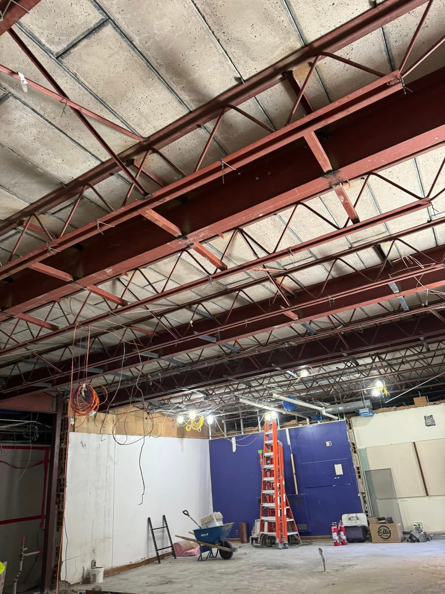 Interior construction view with exposed red steel beams and a ladder against a blue wall.