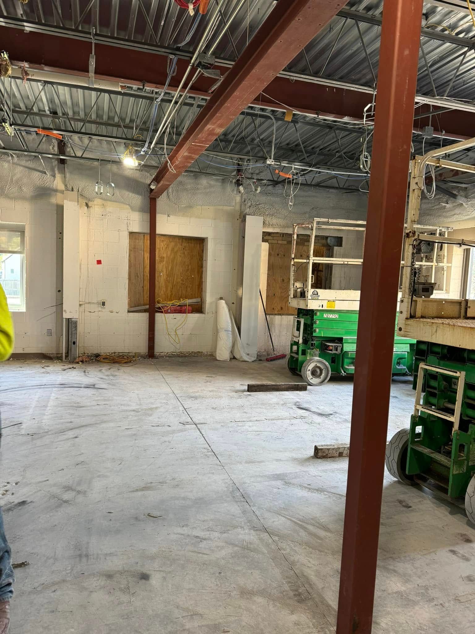 Interior construction site with exposed beams, concrete floor, drywall, and two green lifts.