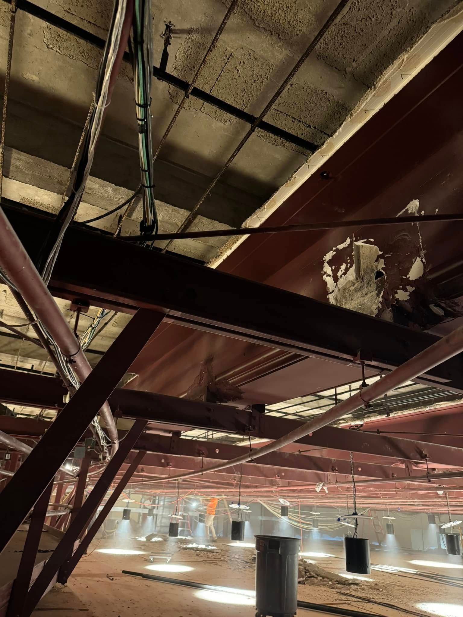 Red steel beams and pipes in a warehouse ceiling; round lights illuminate the floor below.