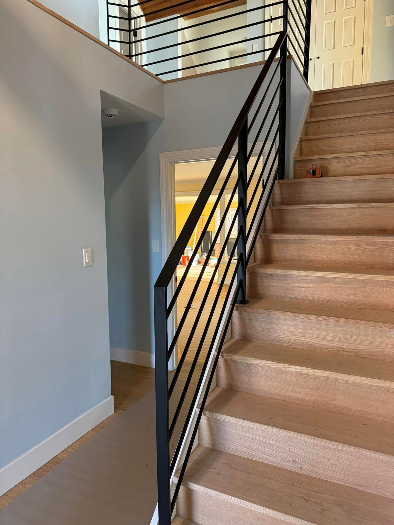 Staircase with black metal railing, light tan carpeted steps, and blue wall.
