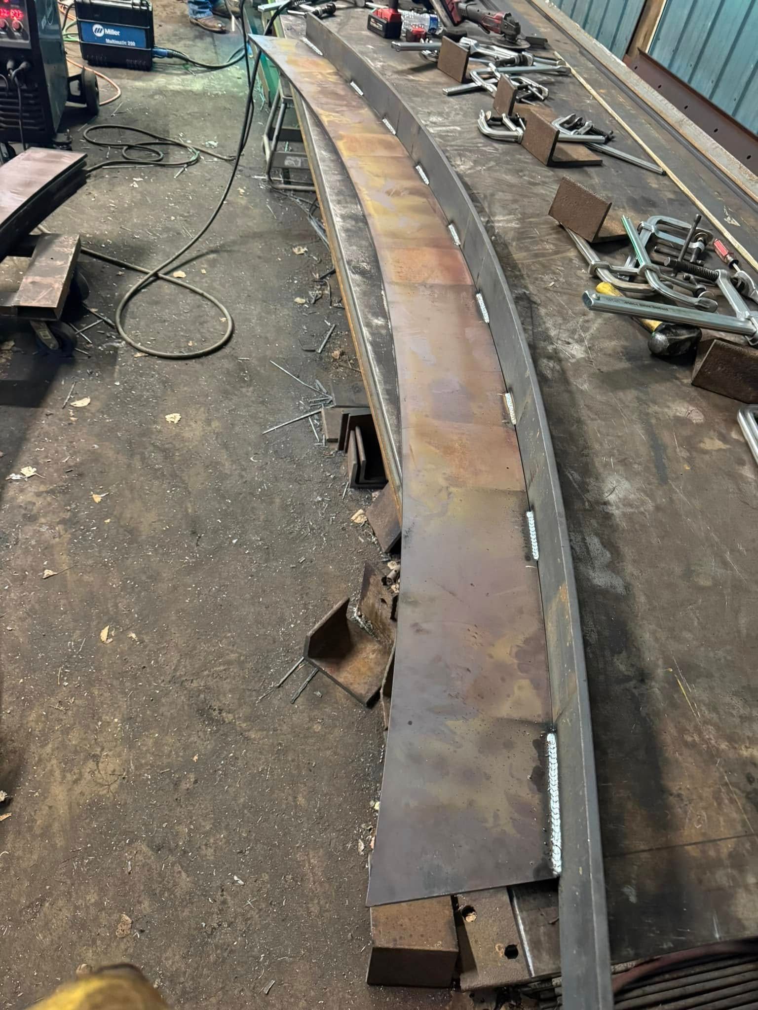Steel metal curved structure in a workshop setting. Welding appears in progress.