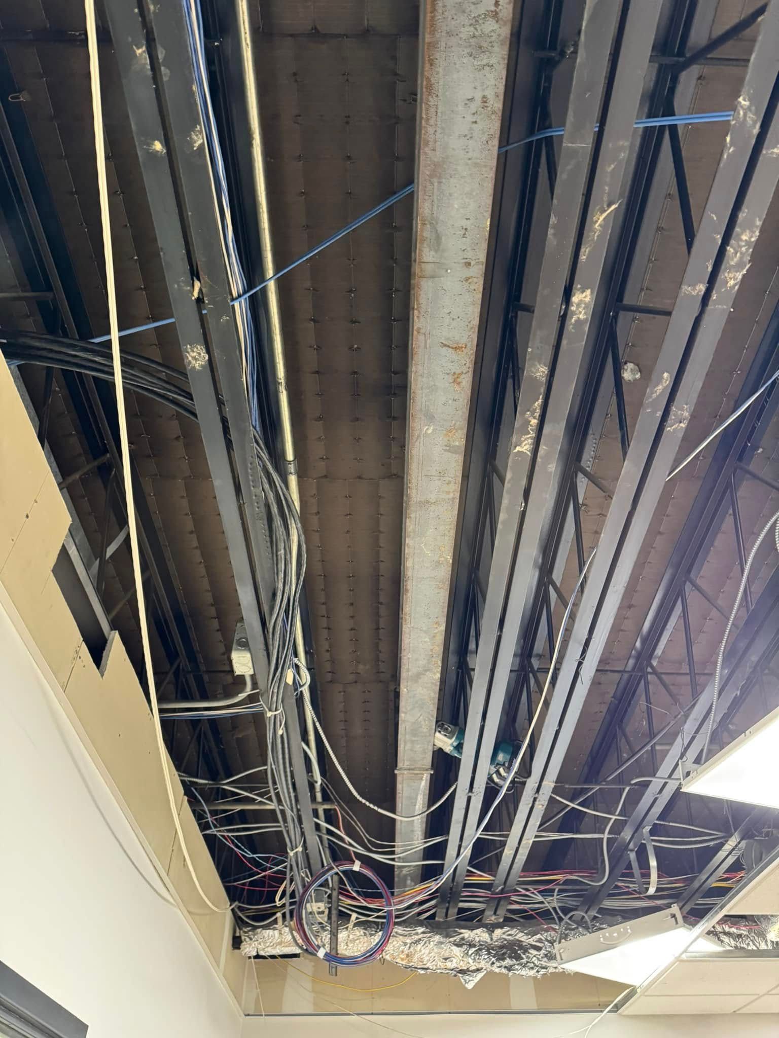 Exposed ceiling infrastructure with metal beams, wires, and damaged panels.