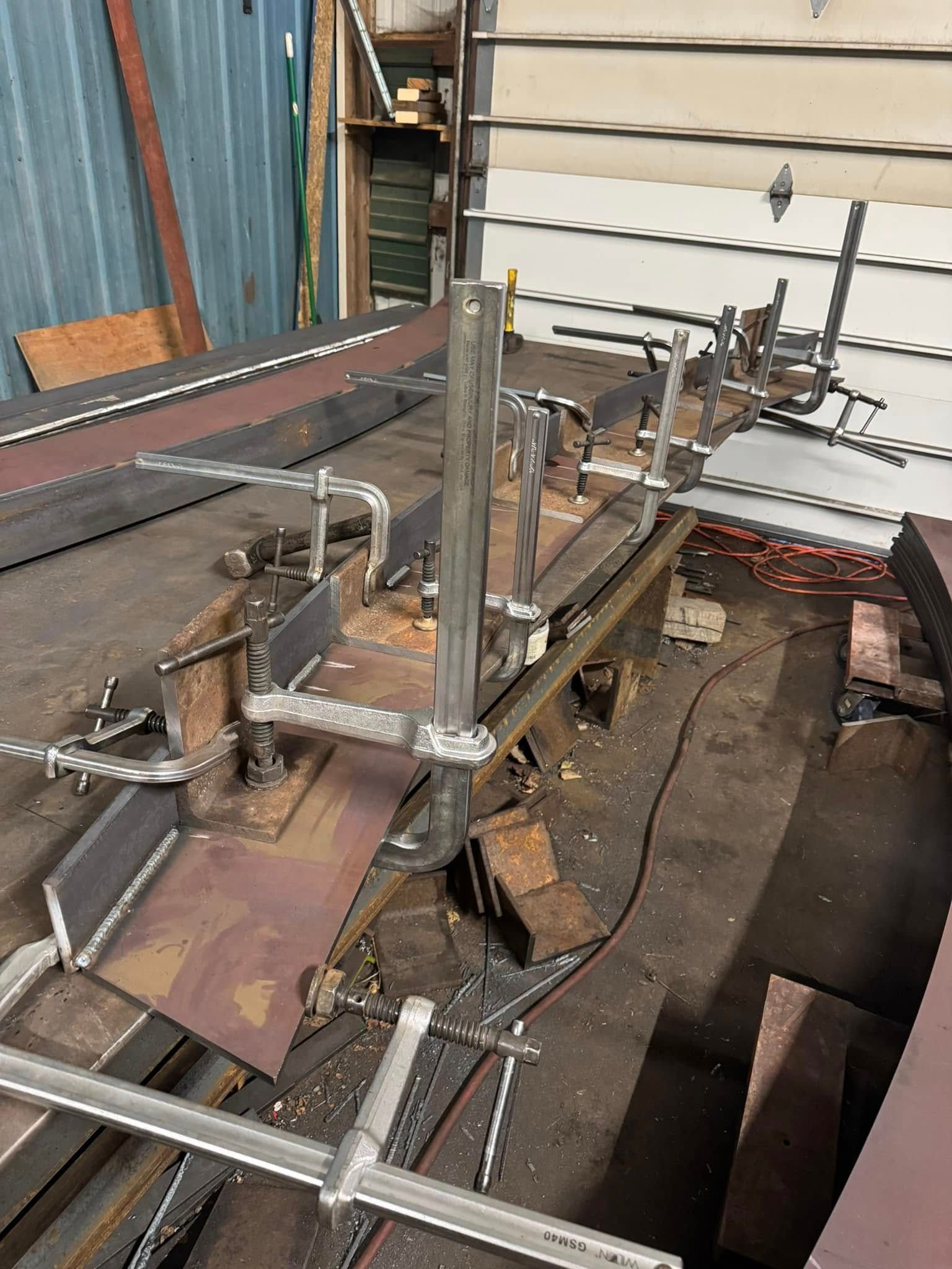 Steel fabrication with clamps securing metal pieces. Workshop setting with welding sparks and tools.