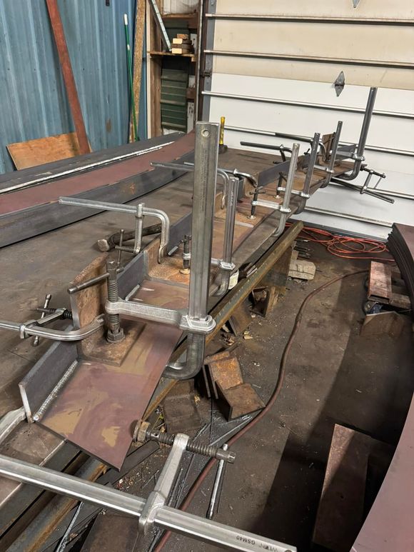 Welding setup: metal pieces clamped and welded in a workshop; various tools and materials visible.