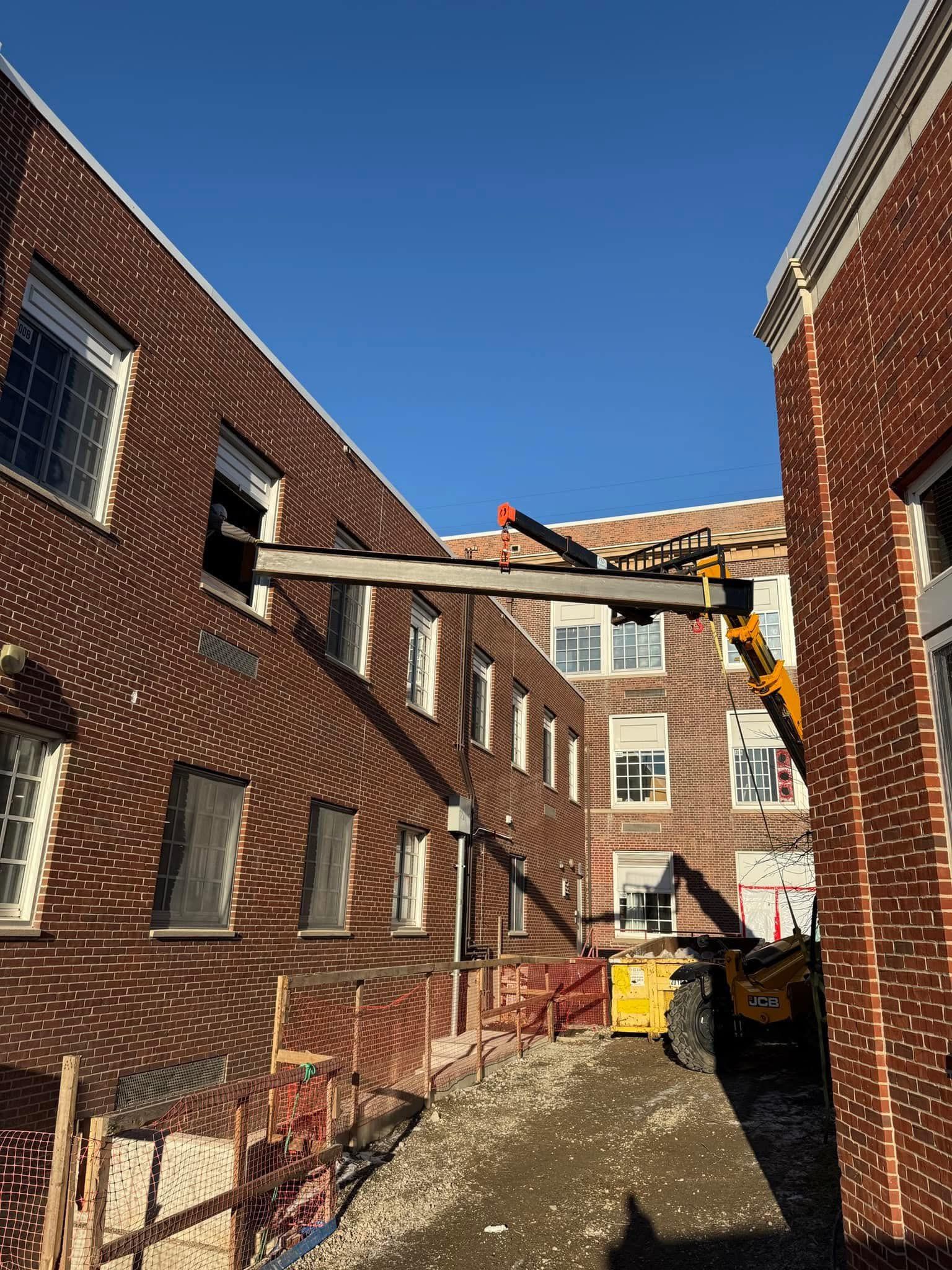 Brick buildings with construction. Steel beam supported by a yellow lift, clear sky.