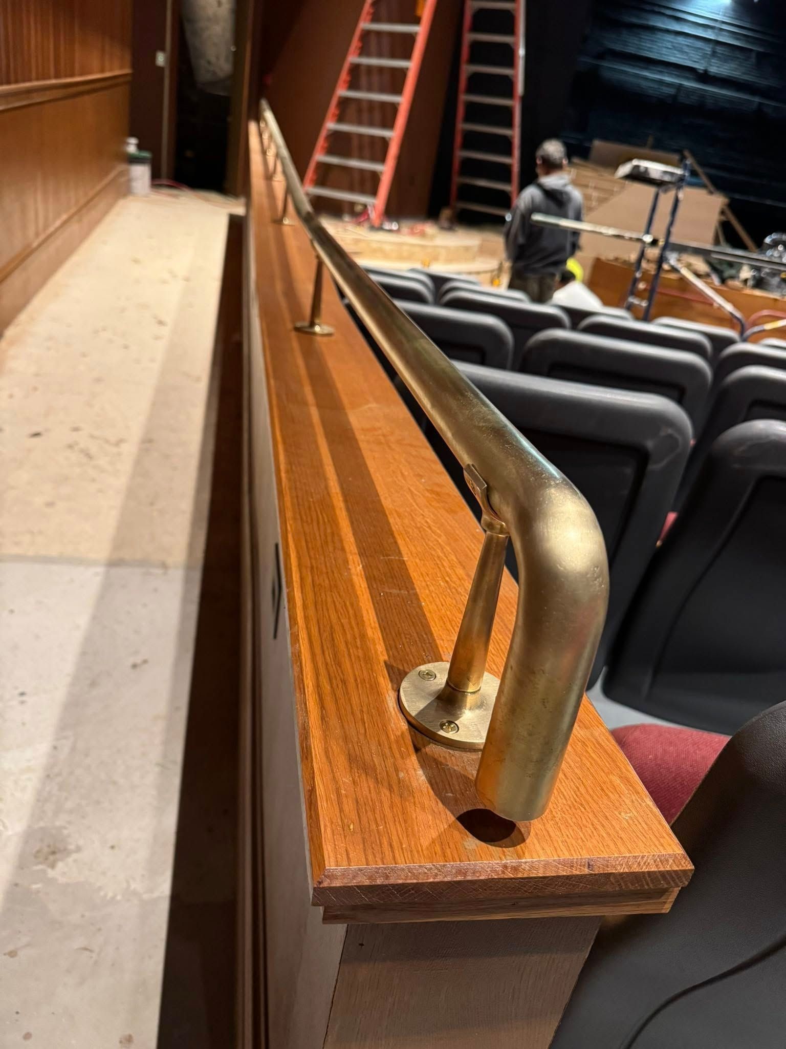 Brass handrail on a wood barrier in a theater under construction; seats visible.