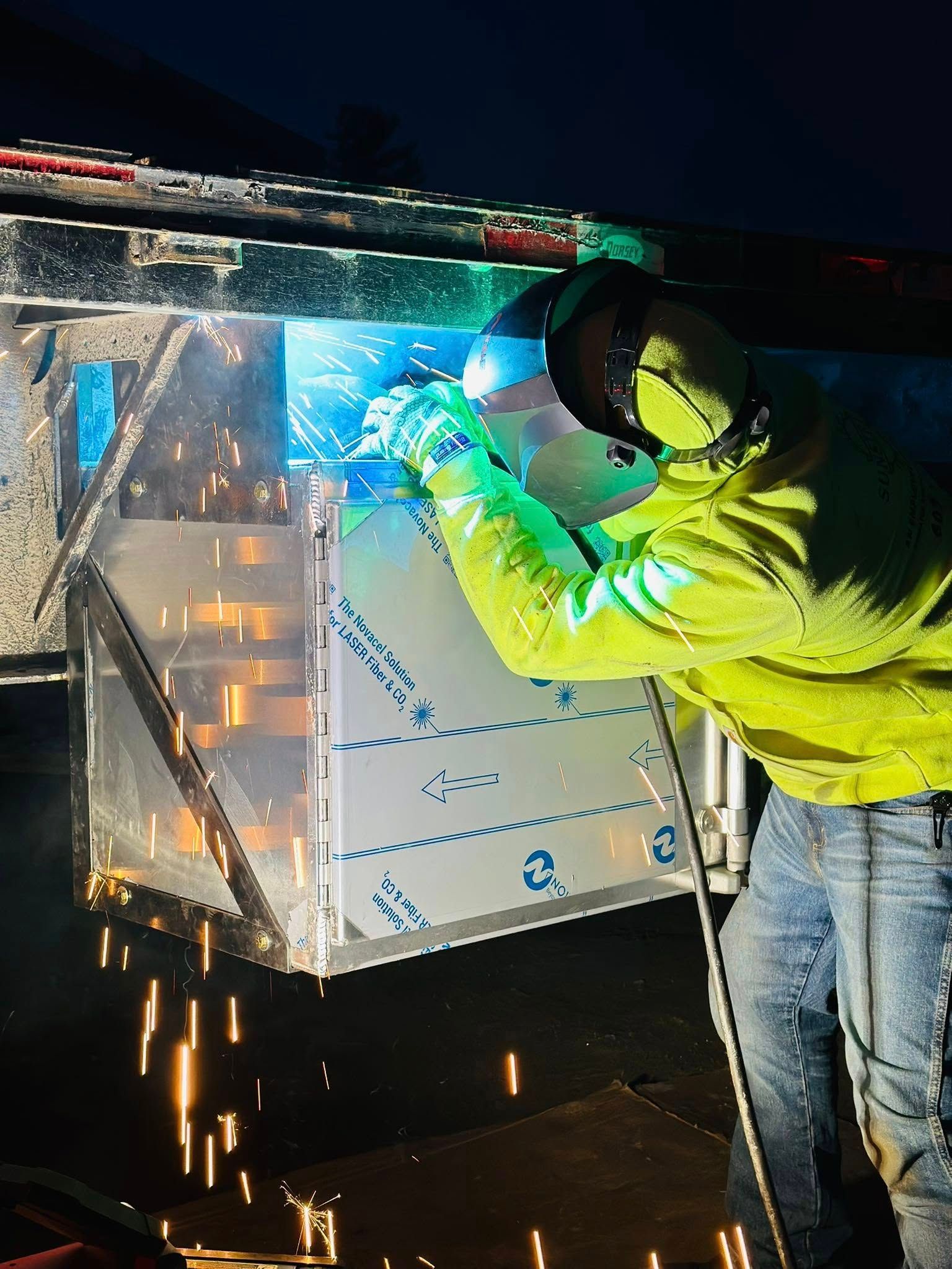 Welder in a protective mask, working on a metal box with sparks flying, at night.