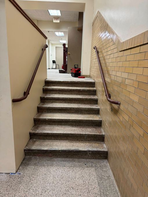 Staircase with textured brick wall, handrails, and tools at the top; interior hallway setting.