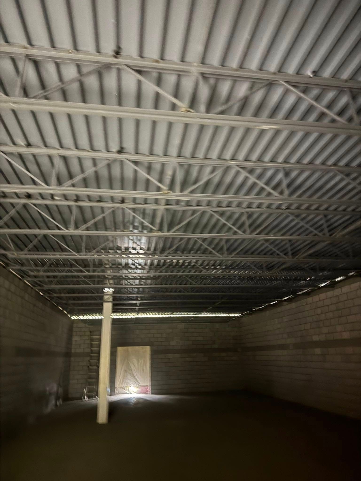 Inside of a building under construction: gray cinder block walls, metal roof structure, and a concrete floor.