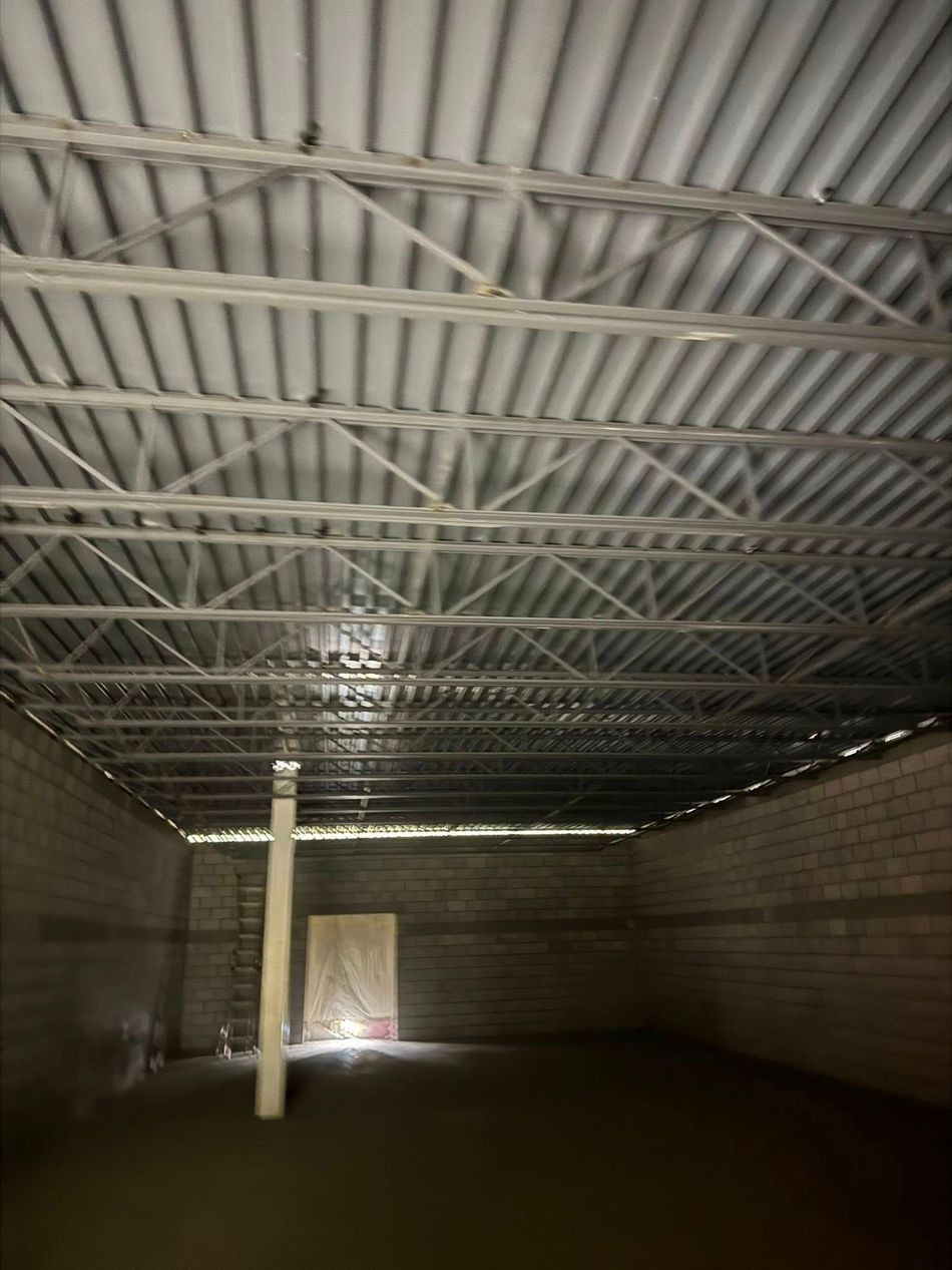 Interior of a building under construction with exposed metal roof supports and concrete block walls.