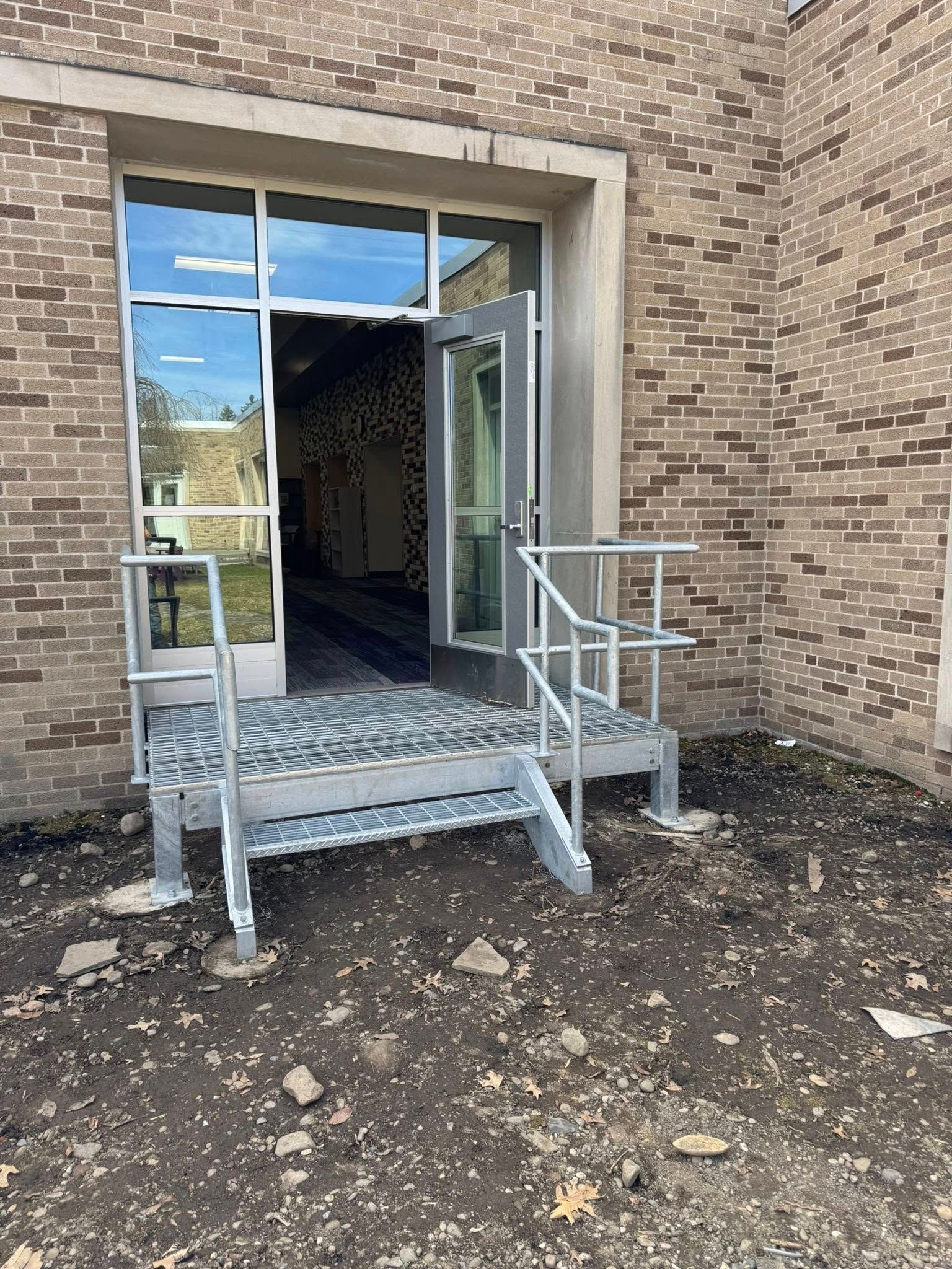 Aluminum ramp and steps leading to a glass door. The building has brick walls.