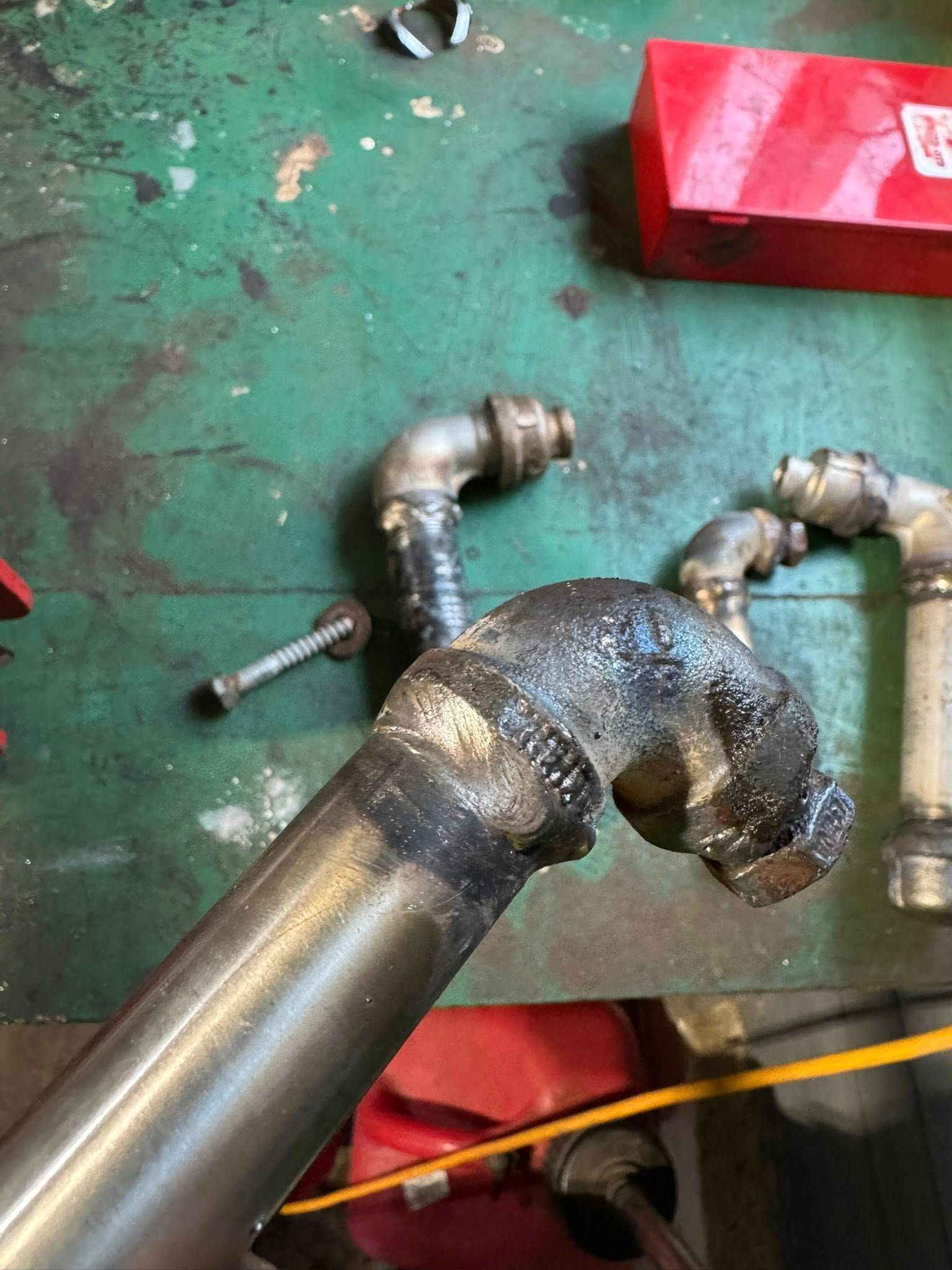 Metal pipes and fittings on a green work surface. One pipe is held, and others are nearby with a bolt.