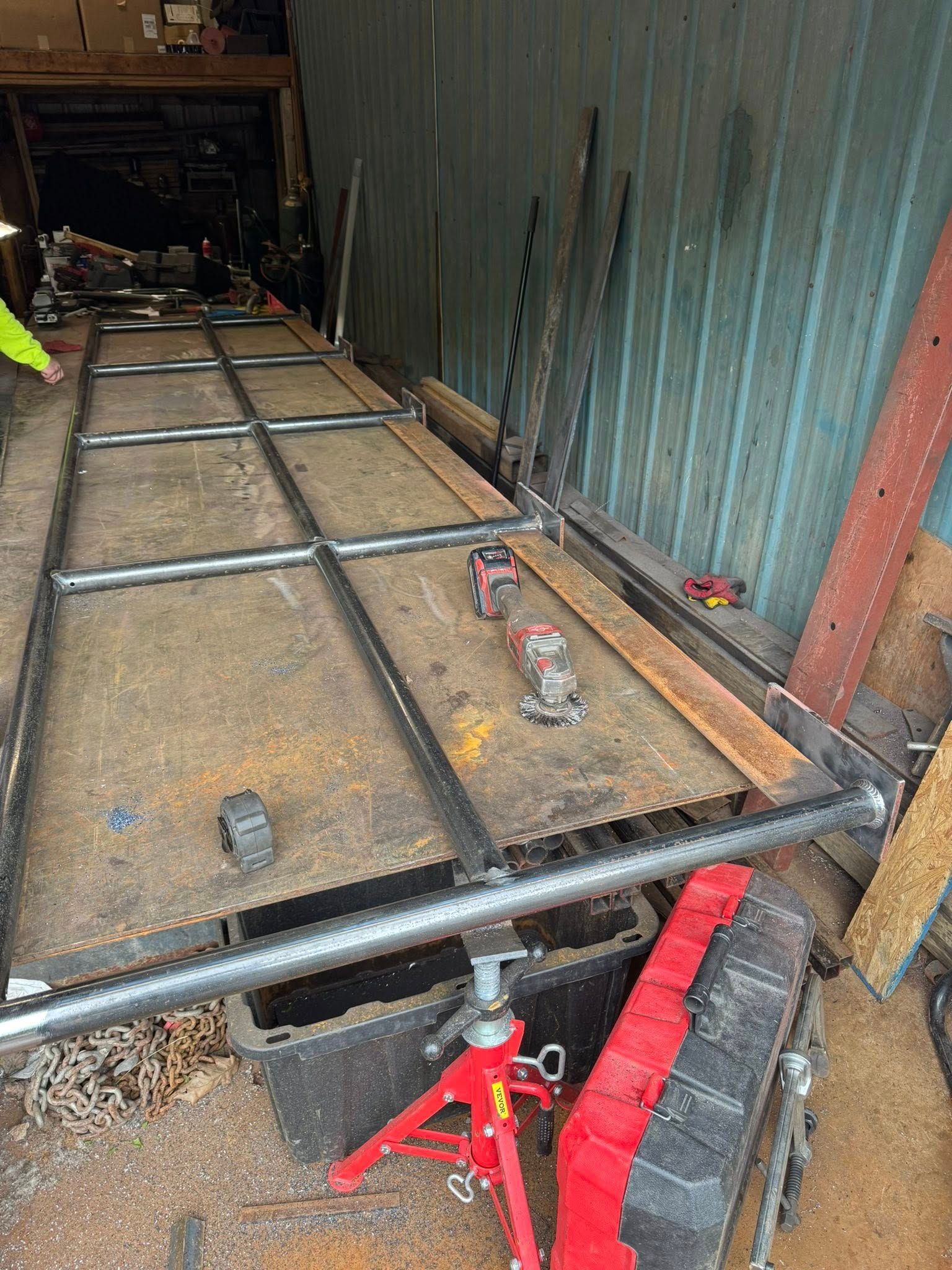 Metal frame being welded on a rusty workbench. Red jack stands and tools nearby.