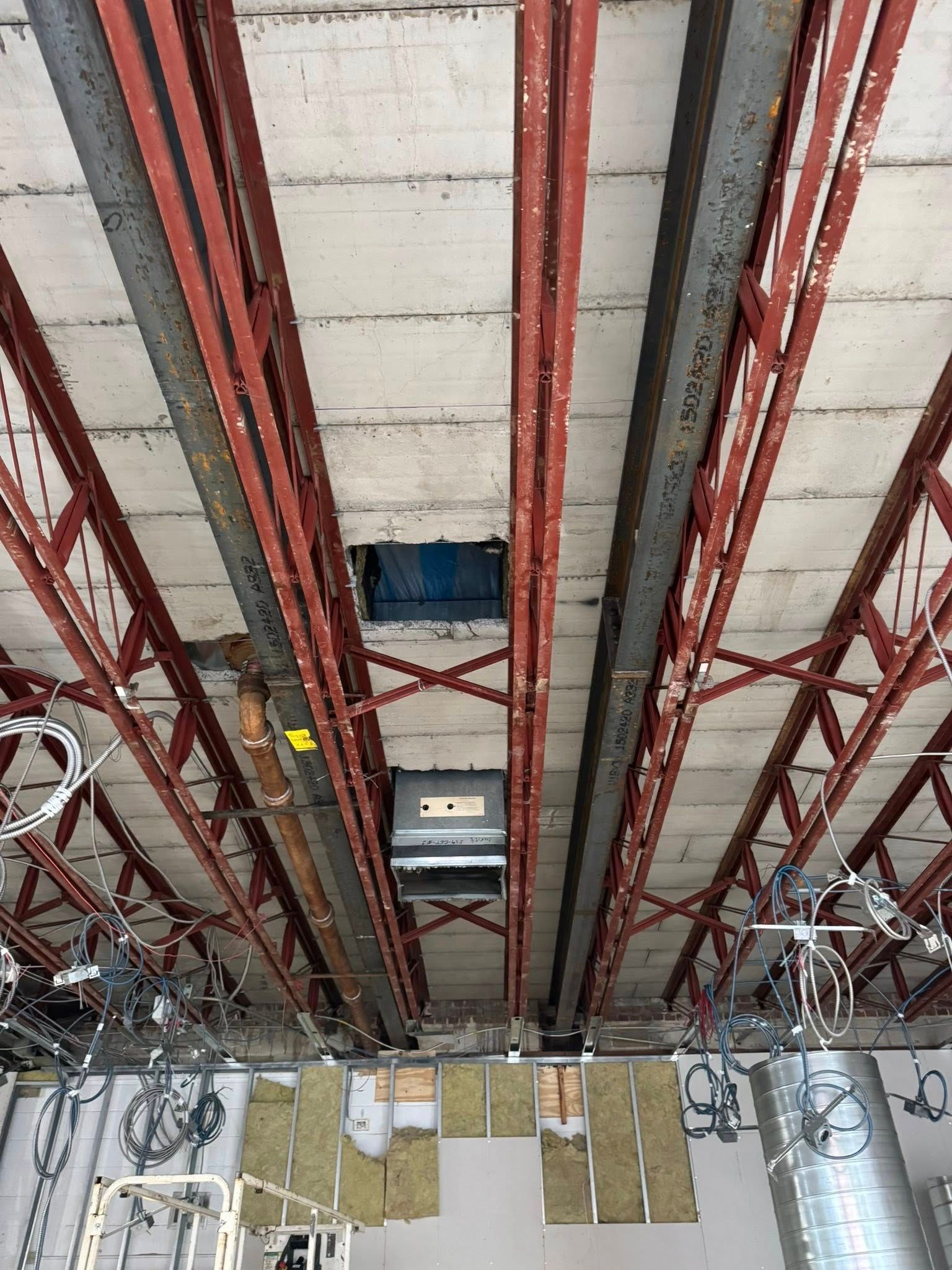 Overhead view of an unfinished building interior, showing exposed red steel beams, concrete panels, and HVAC equipment.