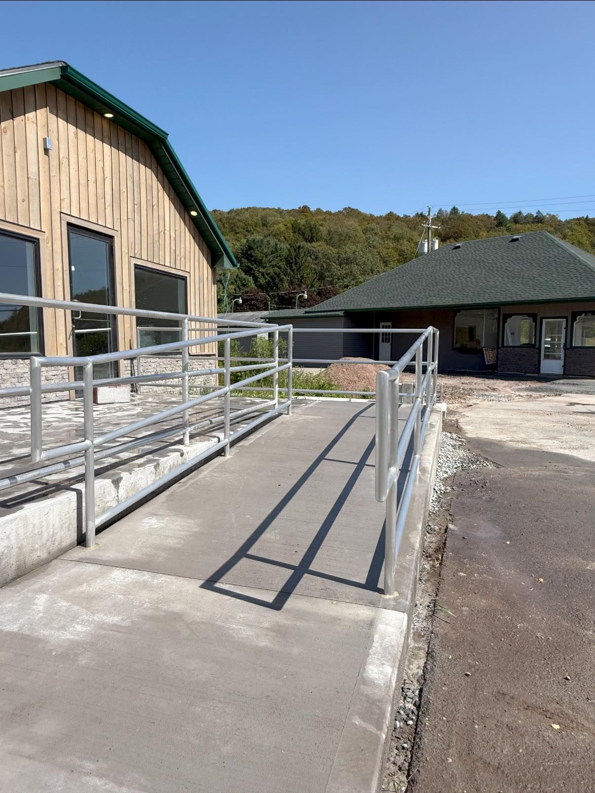 A concrete ramp with silver railings leads to a building with wooden siding and a green roof.